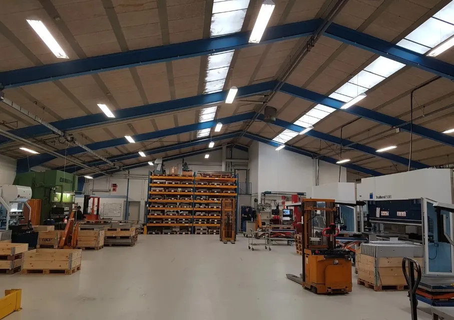 Lagerhallen indeholder flere maskiner og lagerhylder med varer og materialer