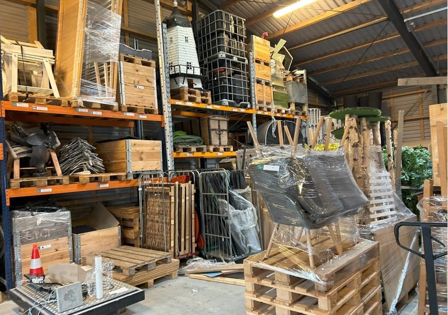 Lager med masser af diverse trækasser, plastposer, stolpe og rullebånd samt en afspærring i højre side.