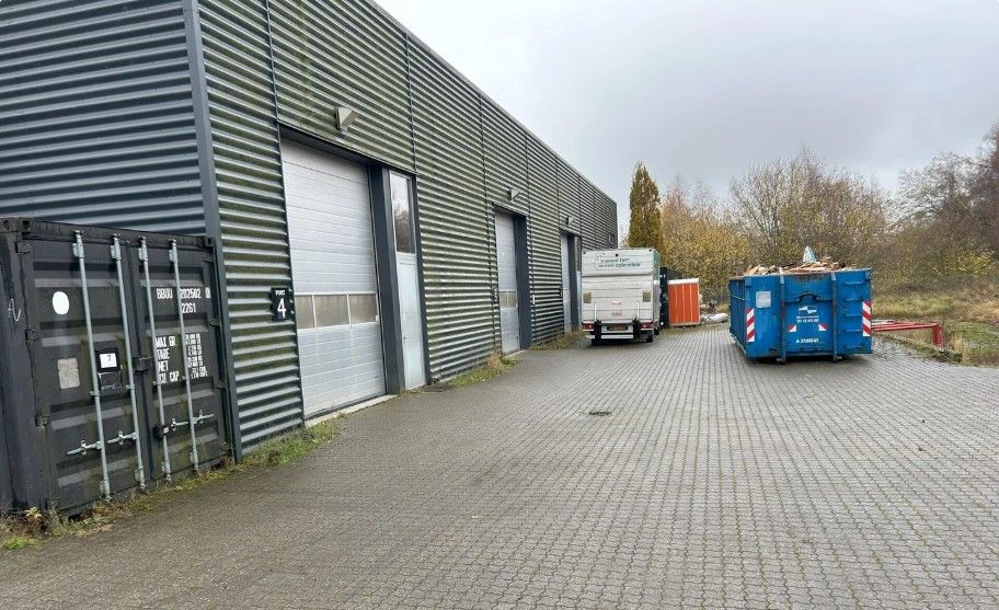 En lastbil parkeret på en vej med to containere og flere lagerbygninger bagved