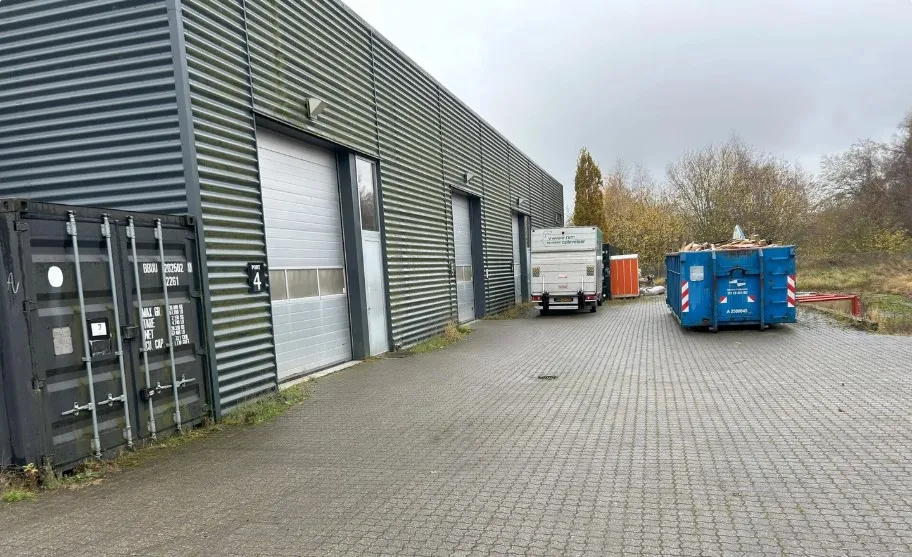 En lastbil parkeret på en vej med to containere og flere lagerbygninger bagved