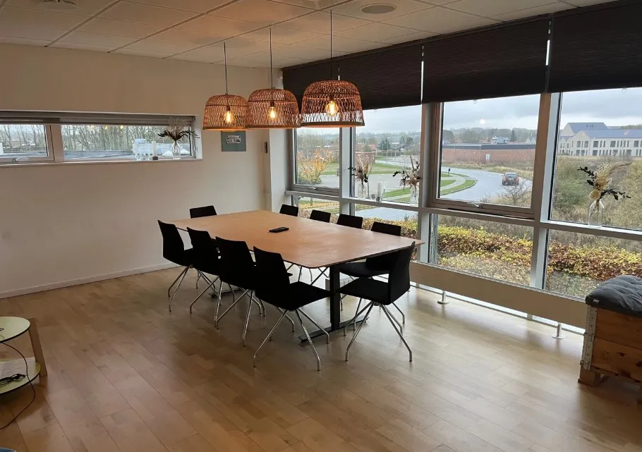 Kontorbord med stole og penge til møder og gruppearbejde i moderne lokaler med store vinduer og udsigt til byen