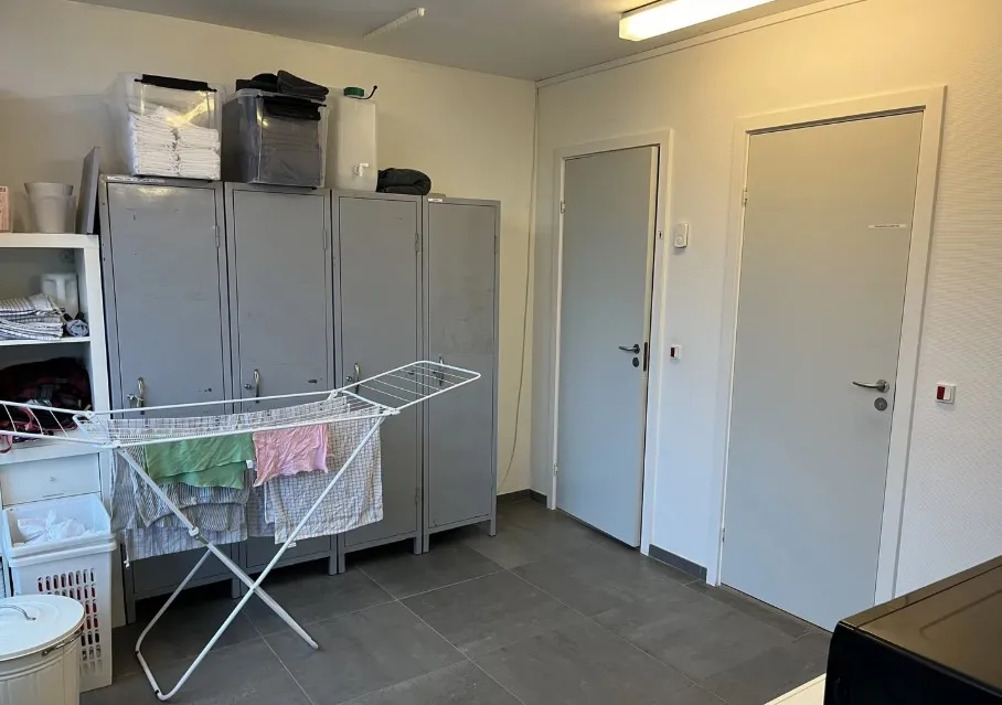 En stor værelse med to hvide døre og loftslampe samt tøjstativet og tøjstativet med tøj og tøjkurve på loftet