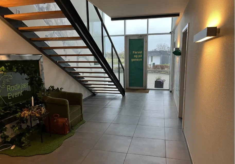 Entrehal med glasdør, grøn væg og lysekroner, hvor der står Farvel og paa gensyn.