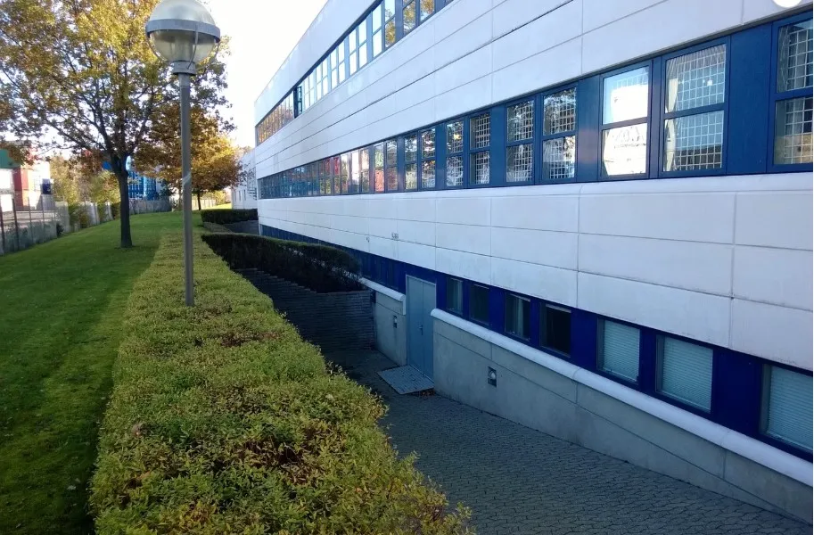 Kontorbygning med lyseblå rammer og mange vinduer, buske og en lampestolpe i forgrunden