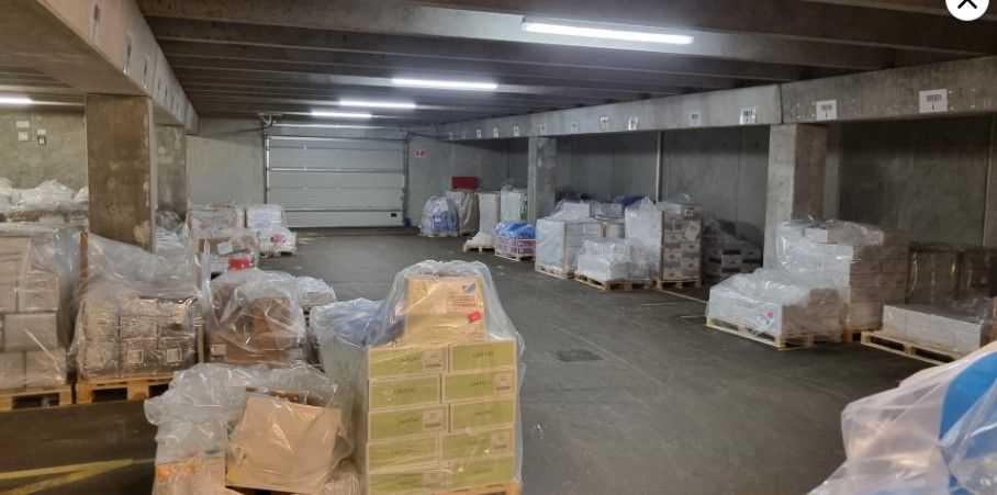 En stor lagerhal fyld med pakket varer, der er dækket med plastfolie, og lagerpallerne er sammen med forskellige varer