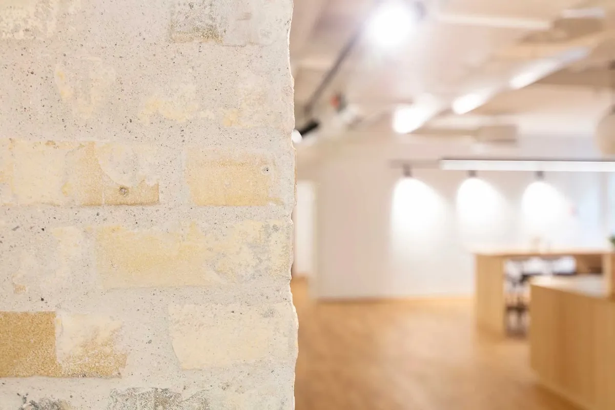 Transparent kontorhus med højt til loftet og lyse loftslampe. Mur med forskellige farvede teglsten og massiv gulvbelægning.