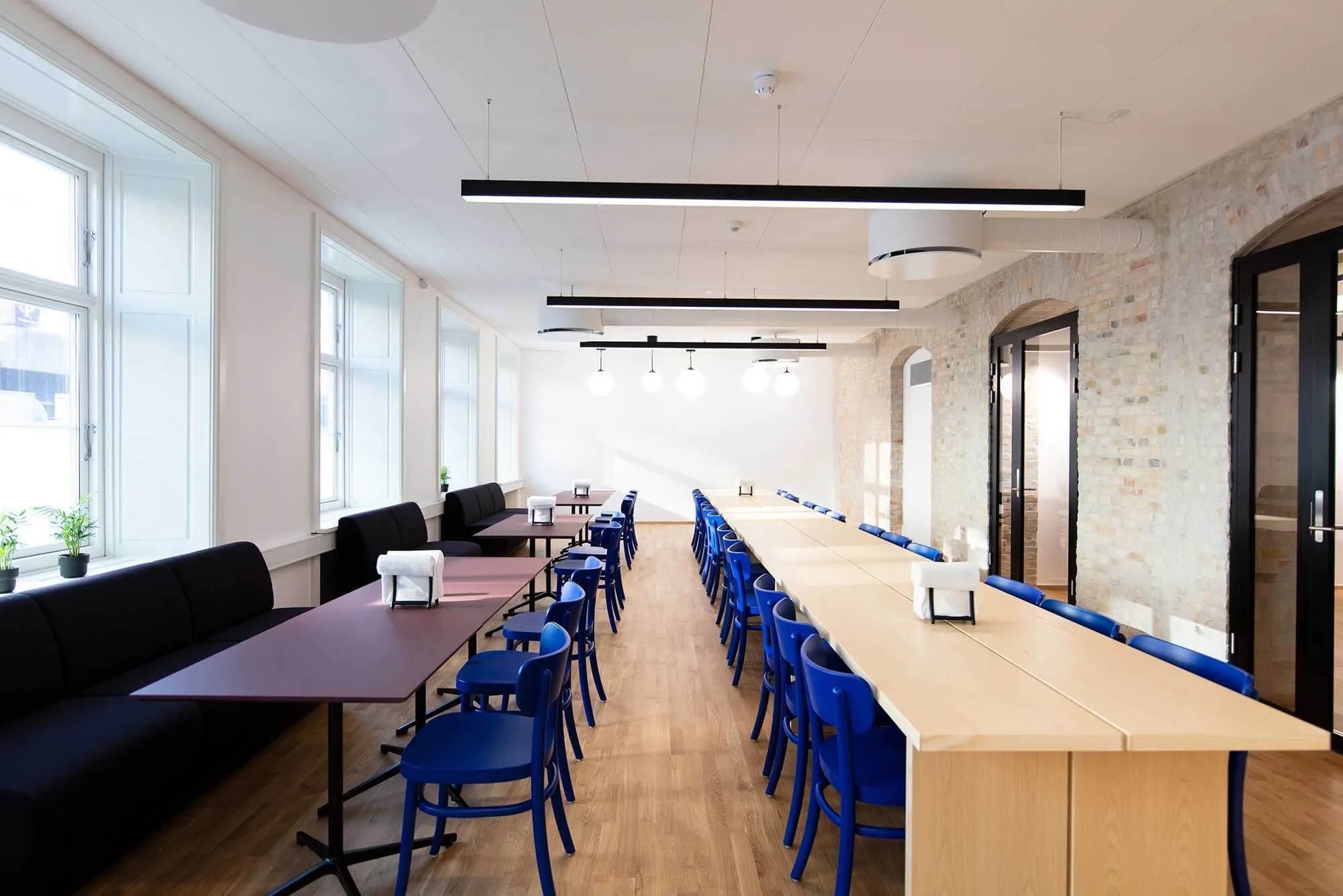 Indvendigt kontor med højt til loftet, hvide vægge, store vinduer, møbler og lysekroner i loftet, samt trægulve