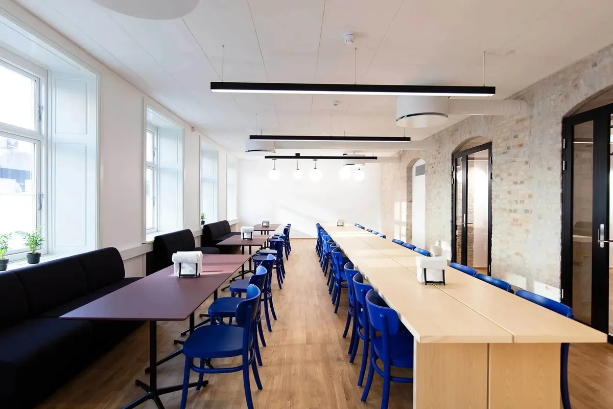 Indvendigt kontor med højt til loftet, hvide vægge, store vinduer, møbler og lysekroner i loftet, samt trægulve