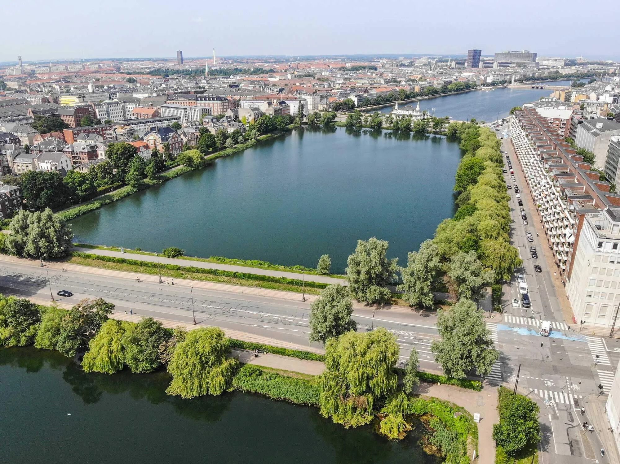 en bred flod med mange bygninger og grønne træer langs bredden, samt en stor by med høje bygninger og tæt trafik på vejen.