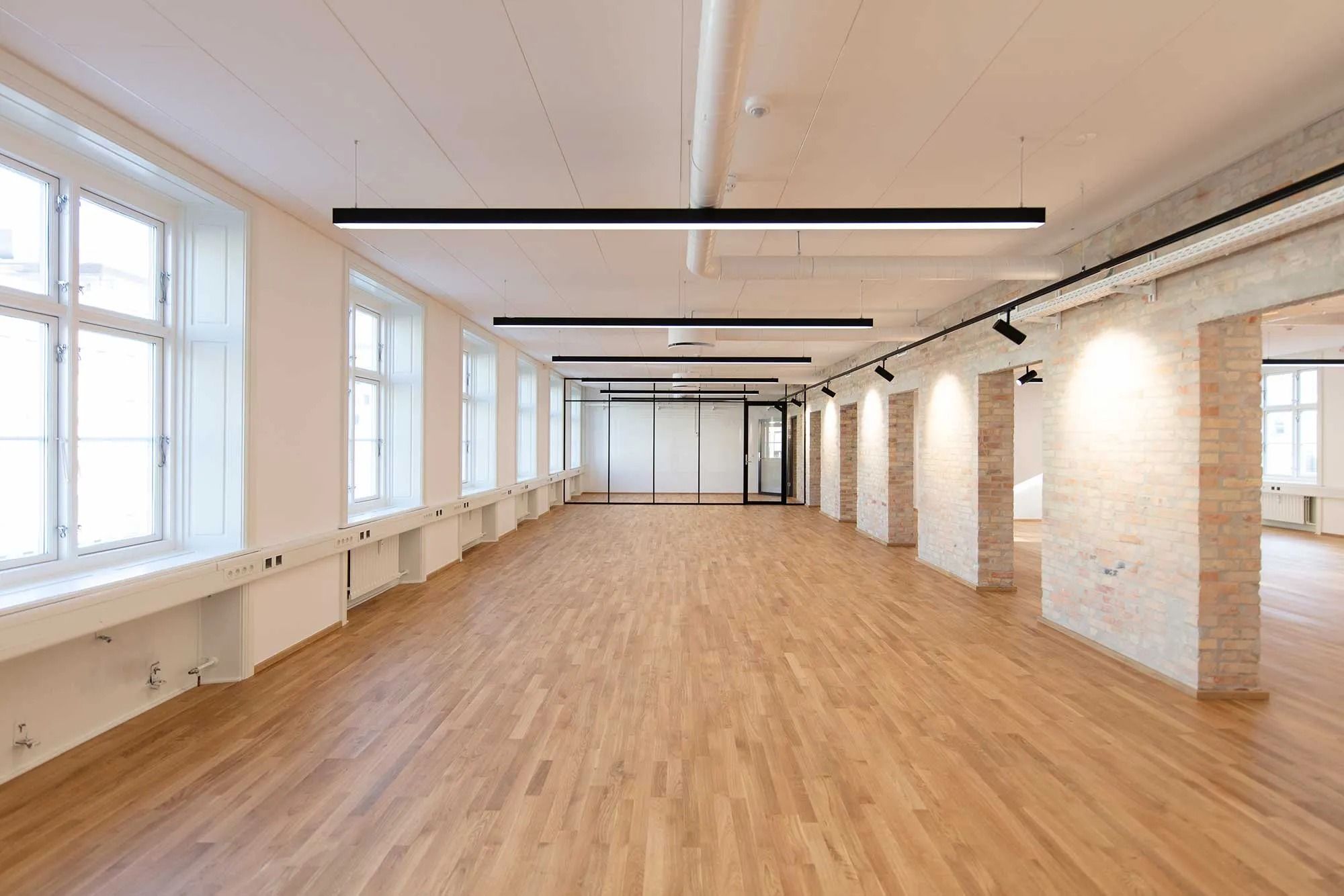 Transparent kontorhus med højt til loftet, hvide vægge, lyse gulvbelægning og stålrør på loftet samt store vinduer