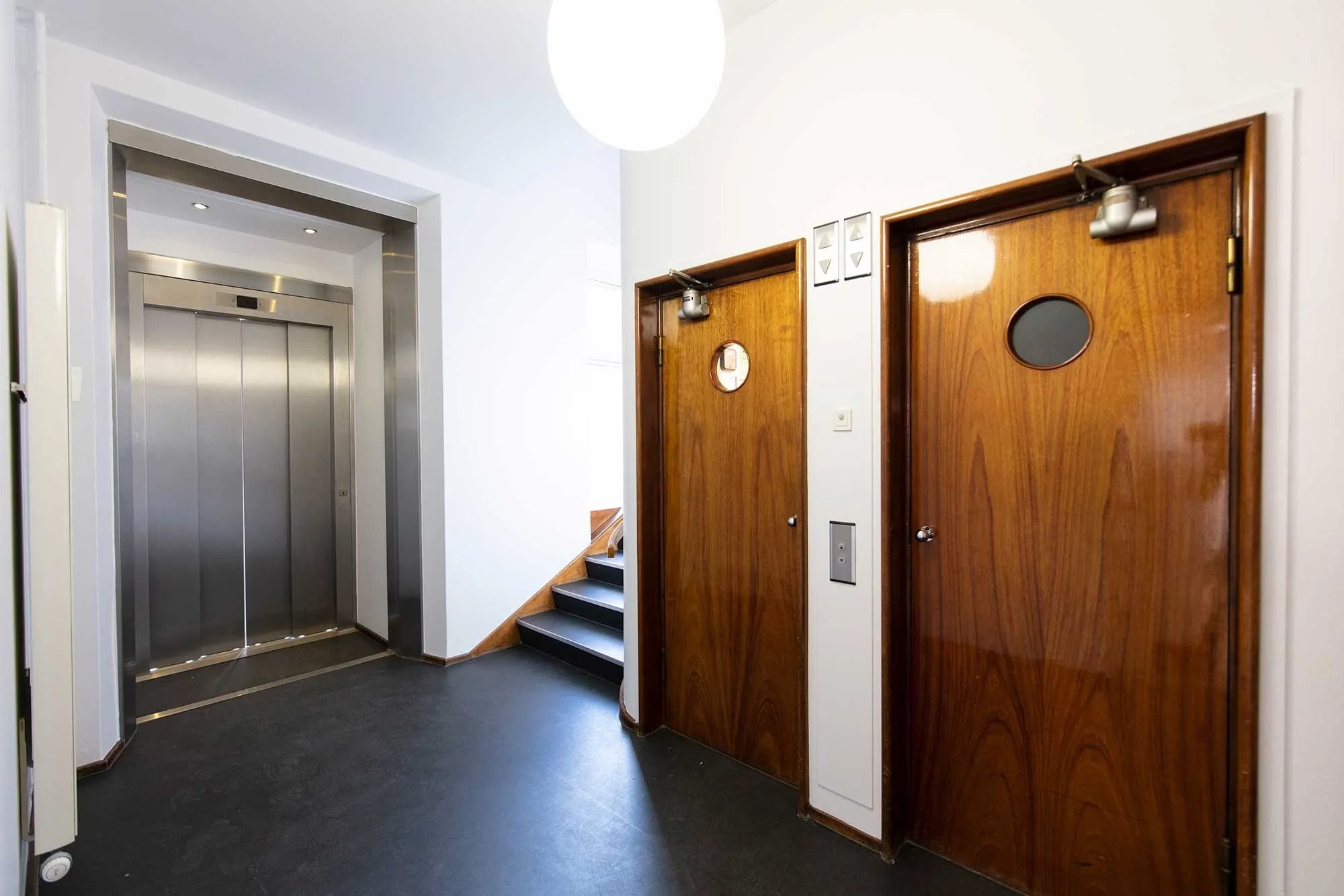 To dore i mørk træ med spejle og tomme elevatorer i baggrunden og et lys på loftet