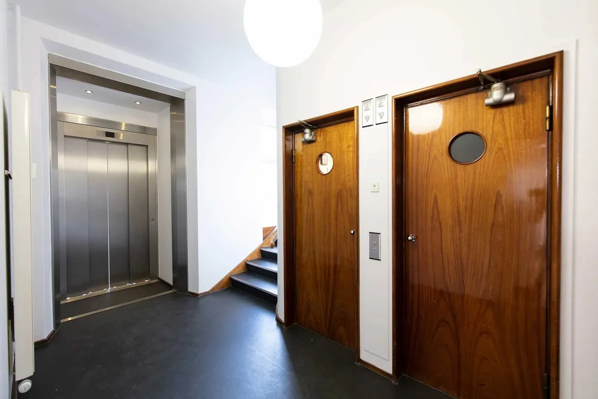 To dore i mørk træ med spejle og tomme elevatorer i baggrunden og et lys på loftet