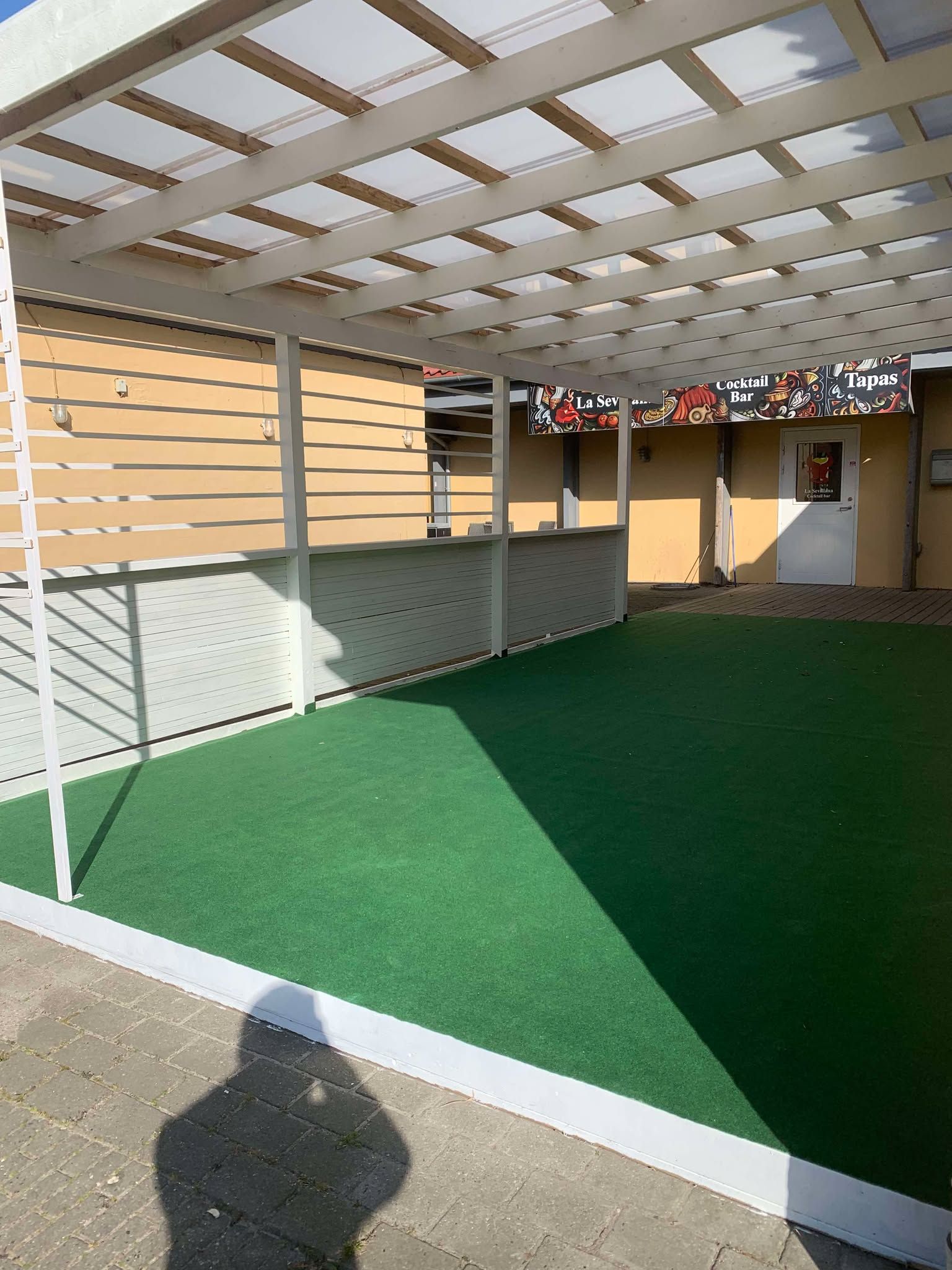 Et luksuriøst restaurantområde med grønt kunstgræs, en hvid pæl og en skurtag over bordene