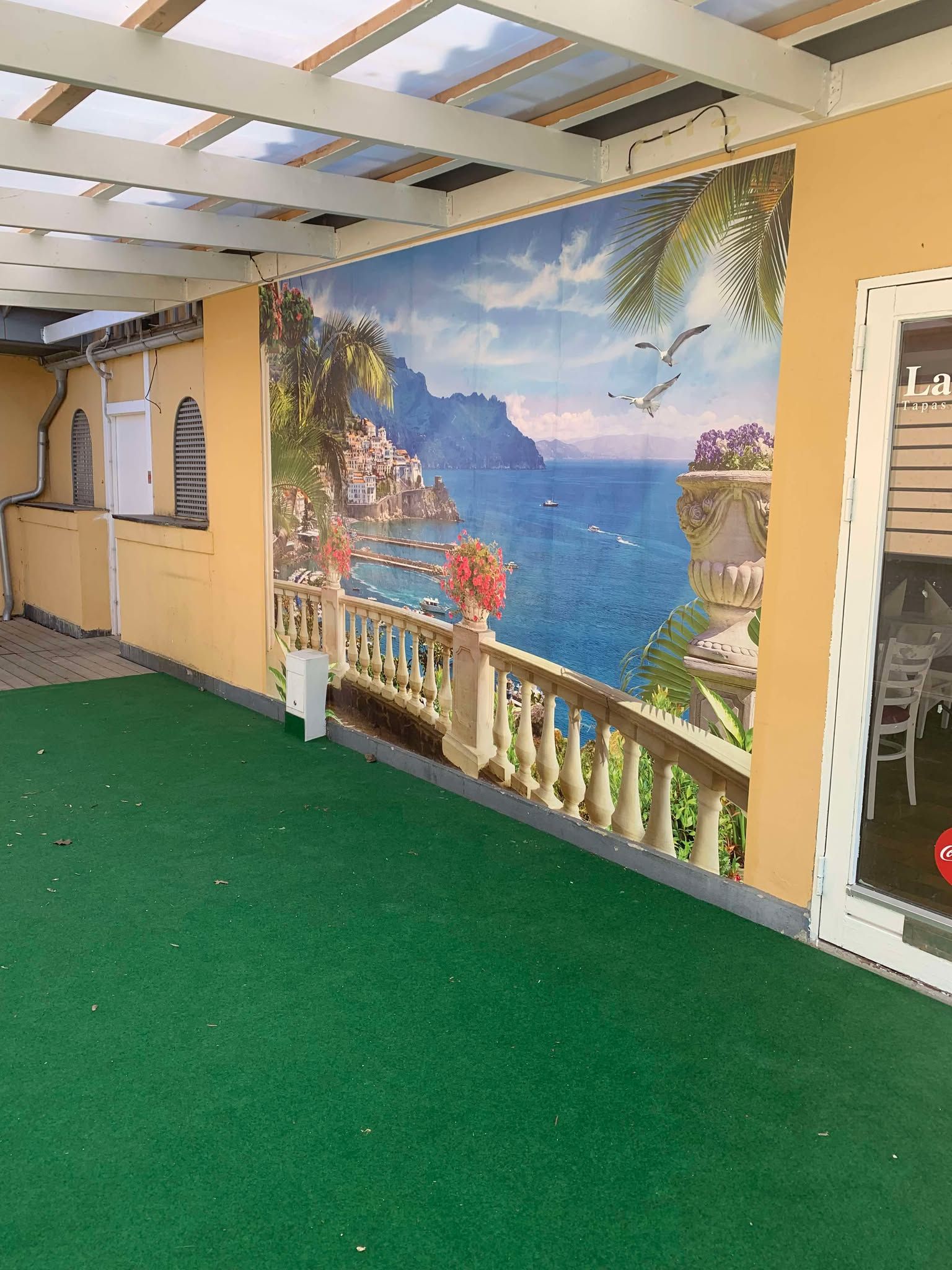 En restaurant med et terrasseområde og en kunstnerisk baggrundsvæg med udsigt til havet og en balkon