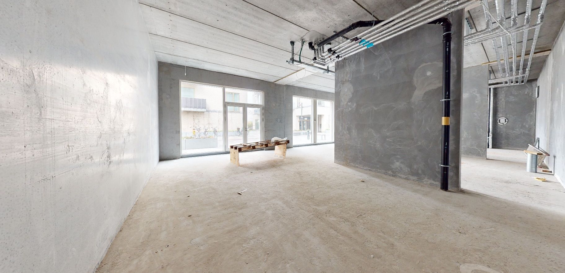 Et ubeboet og ubenyttet lokale med et bænk og to vinduer og et rørsystem og en stålramme i loftet