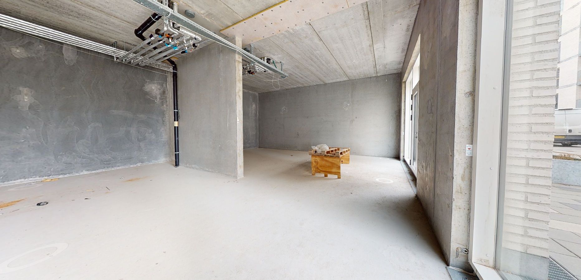 Tom rum med hvid gulv og betonvægge og to små brædtæske i midten med en plastikpose og en kasse ovenpå