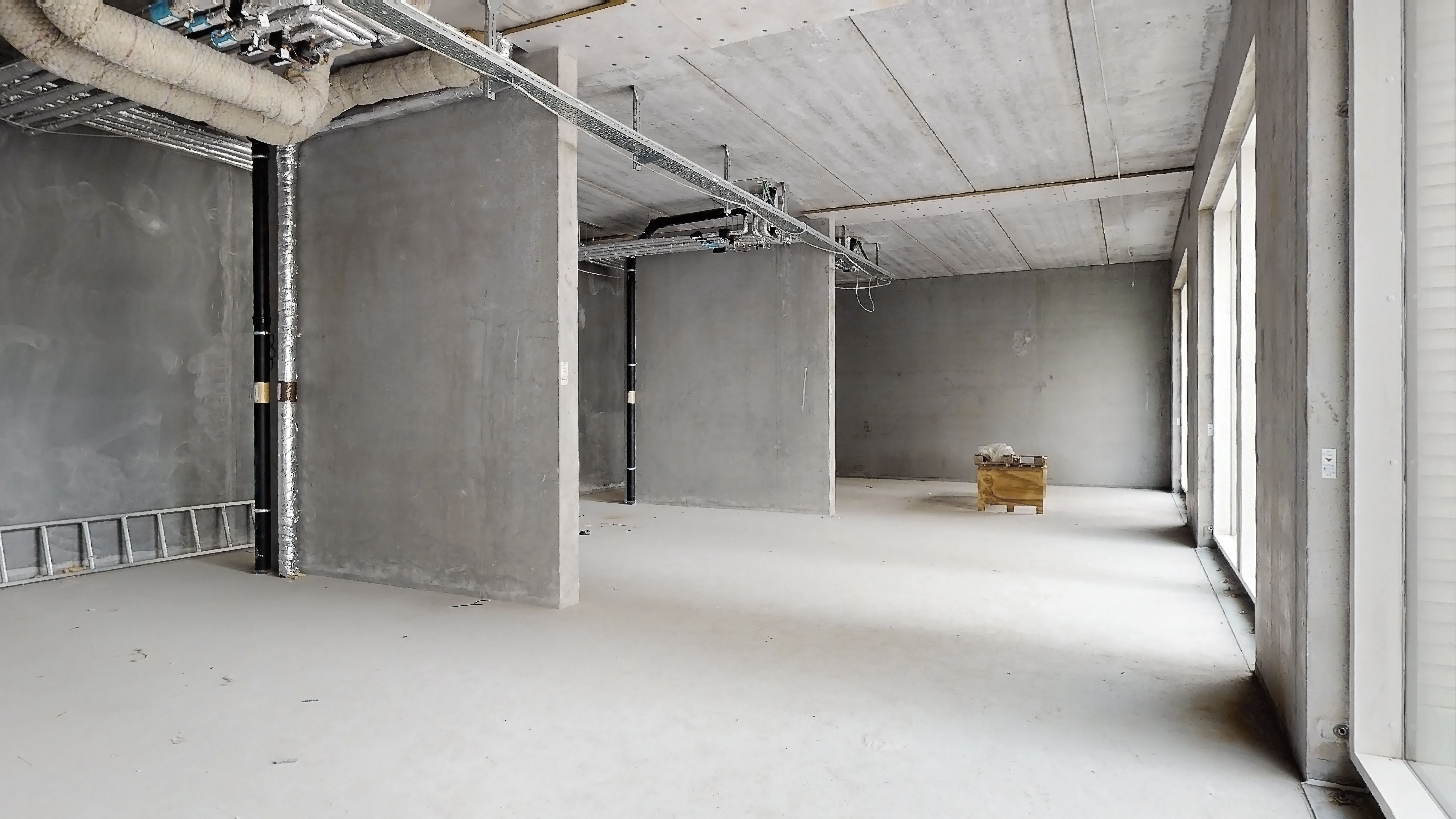 Et værkstedsrum med hvide vægge og gulv samt metalrør og et træskab med materialer