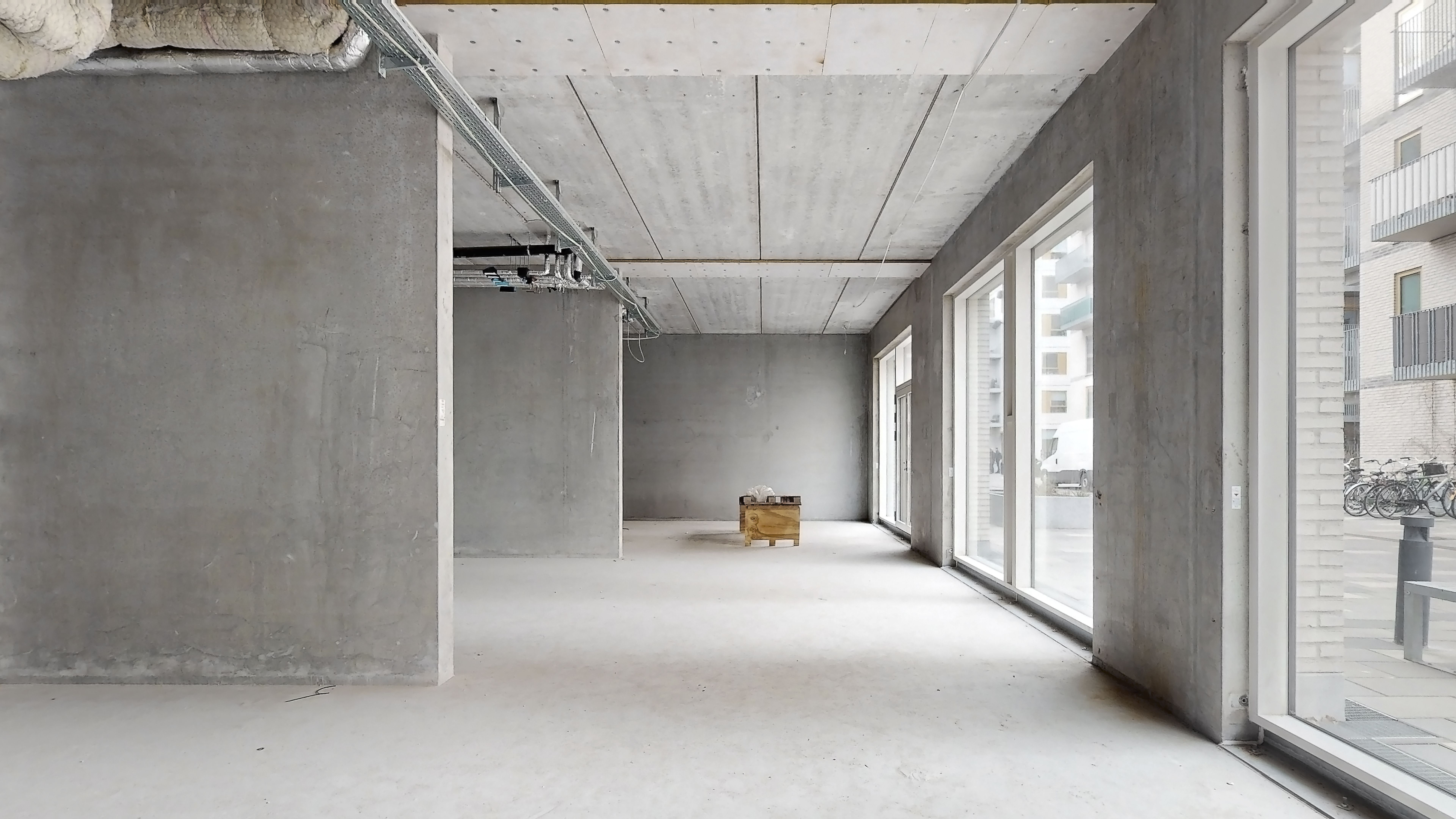 Et rum med lyse gulve, høje vægge og glasvinduer. Der er en trækasse med en kasse ovenpå. Der er røre og materialer på