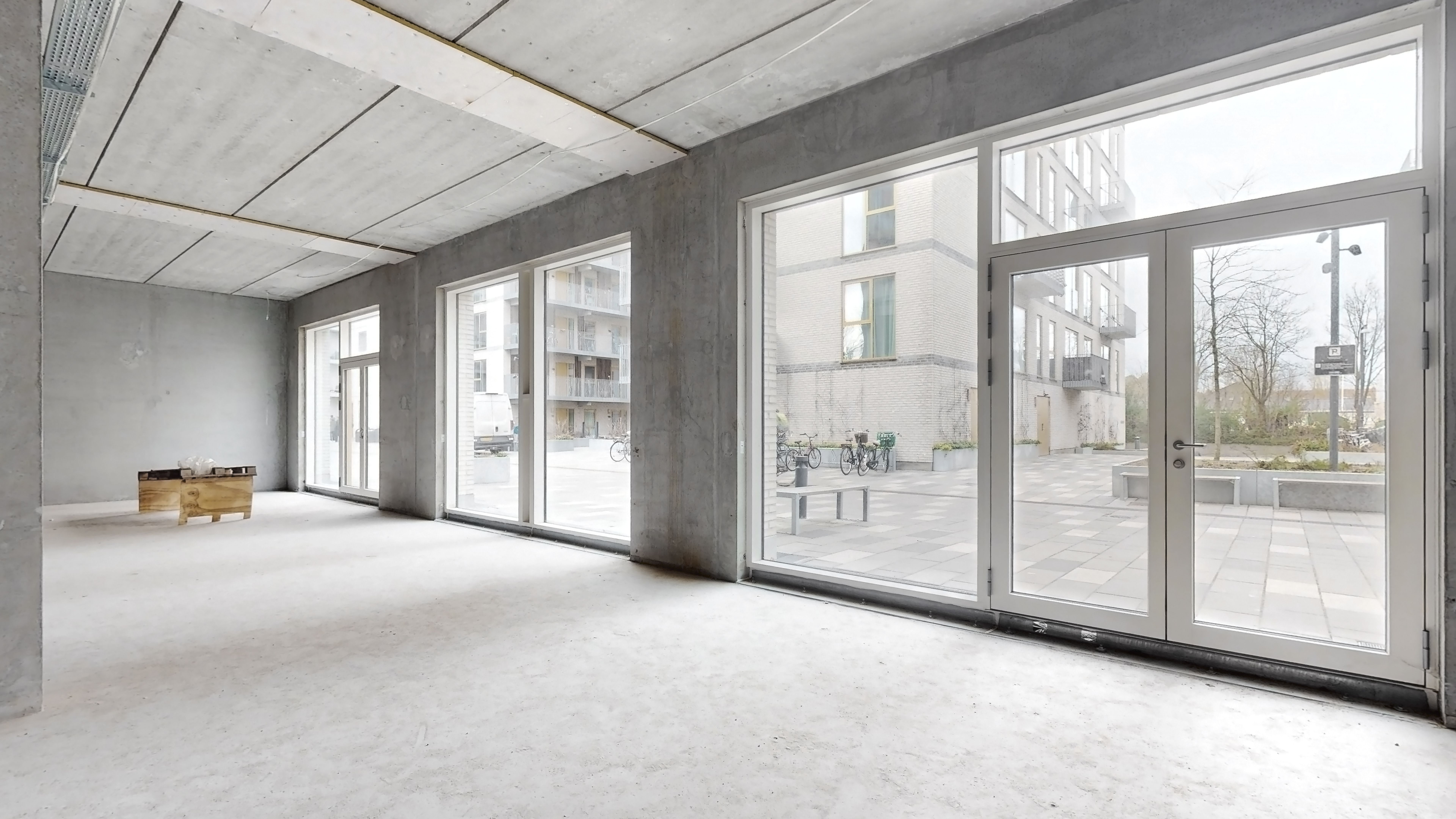 En stor, møbleret lejlighed med højloftede rum og store vinduer mod gårdhave. Parkerede cykler og plantager udenfor