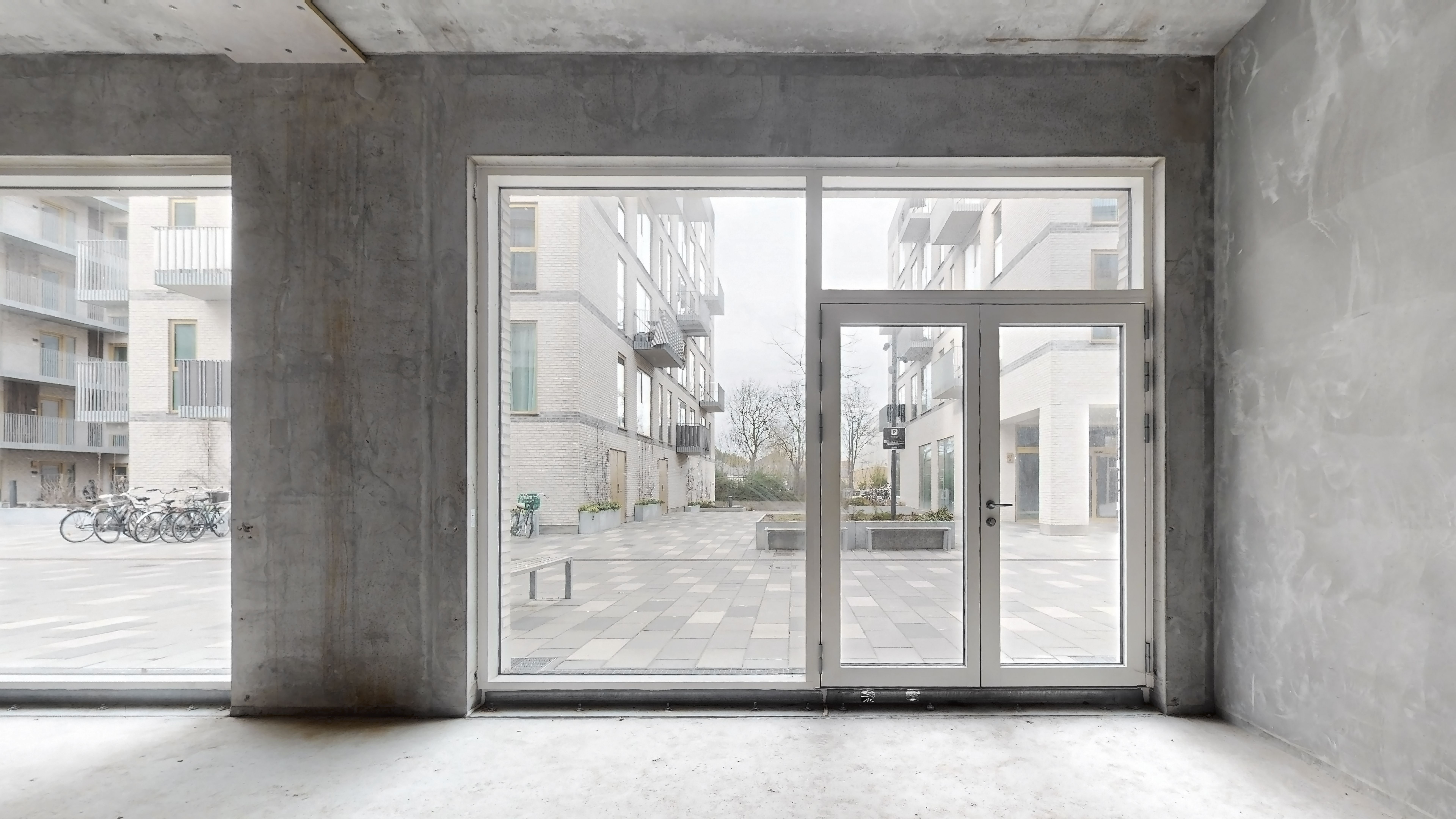 En glasdør og vinduer i en ny bygning med en gård med plantager og cykler og en skov bagved