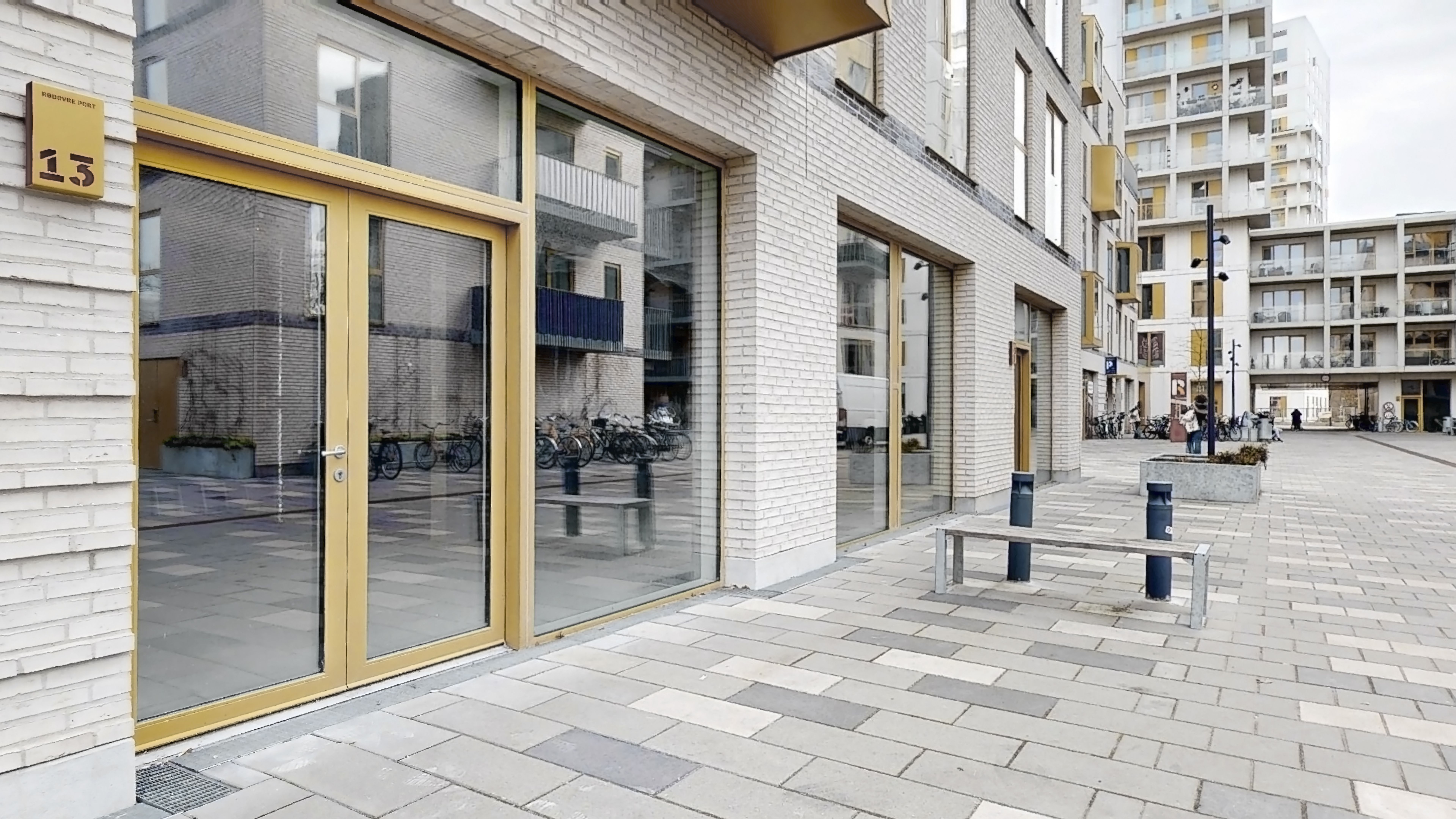 Moderne bygning med store glasdøre og guldfærgede indramninger, foran terrasser med balkoner og søjler