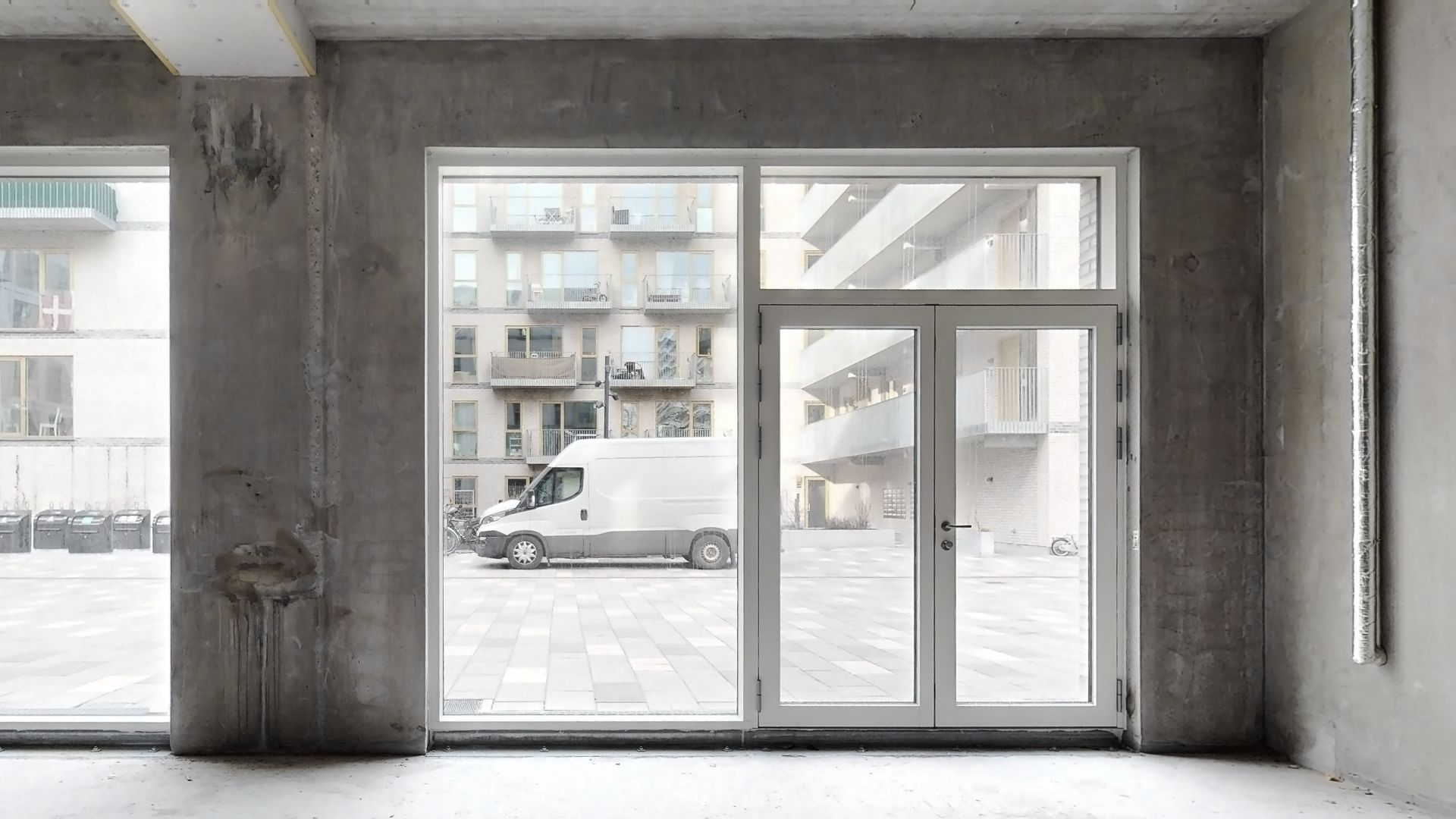 En tom bygning med store vinduer og en hvid lastbil parkeret udenfor på en parkeringsplads