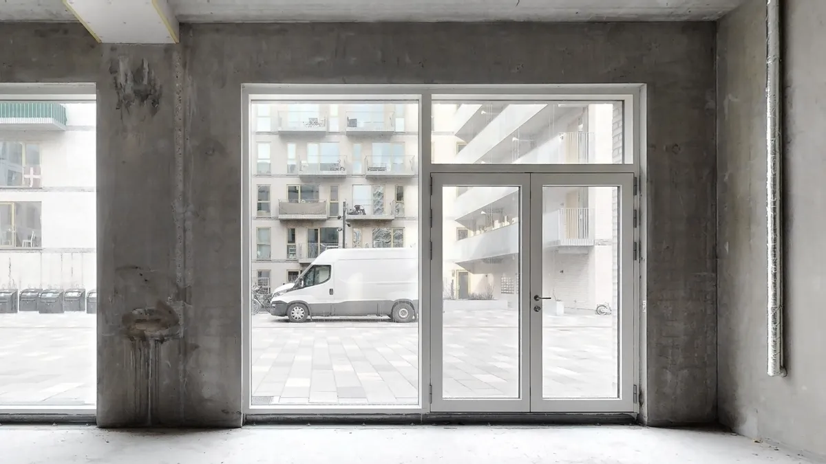 En tom bygning med store vinduer og en hvid lastbil parkeret udenfor på en parkeringsplads