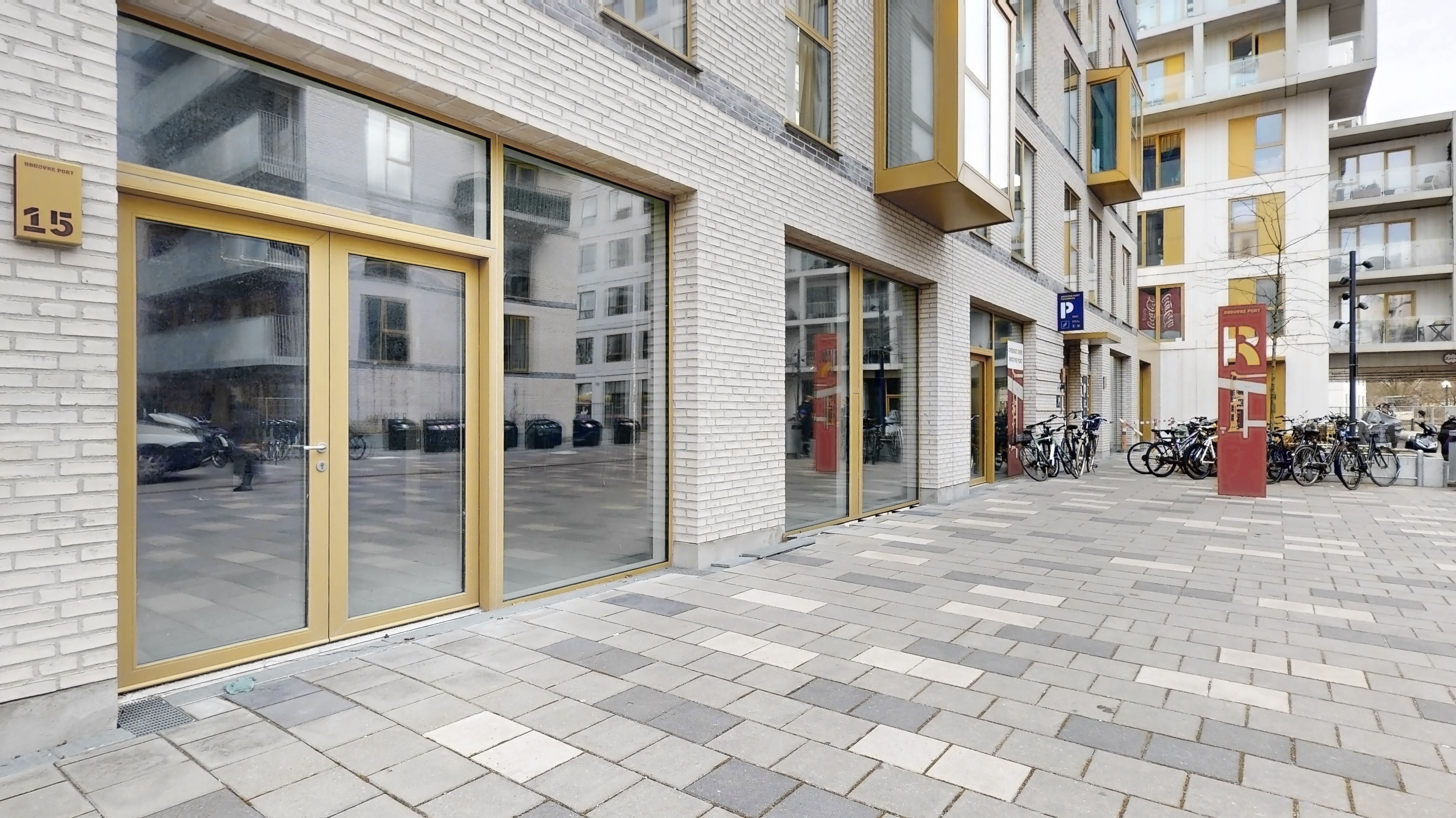 Gammel bydel med moderne facader og glasdøre i Rødovre. En parkeringsplads med flere cykler og bygninger med store vinduer