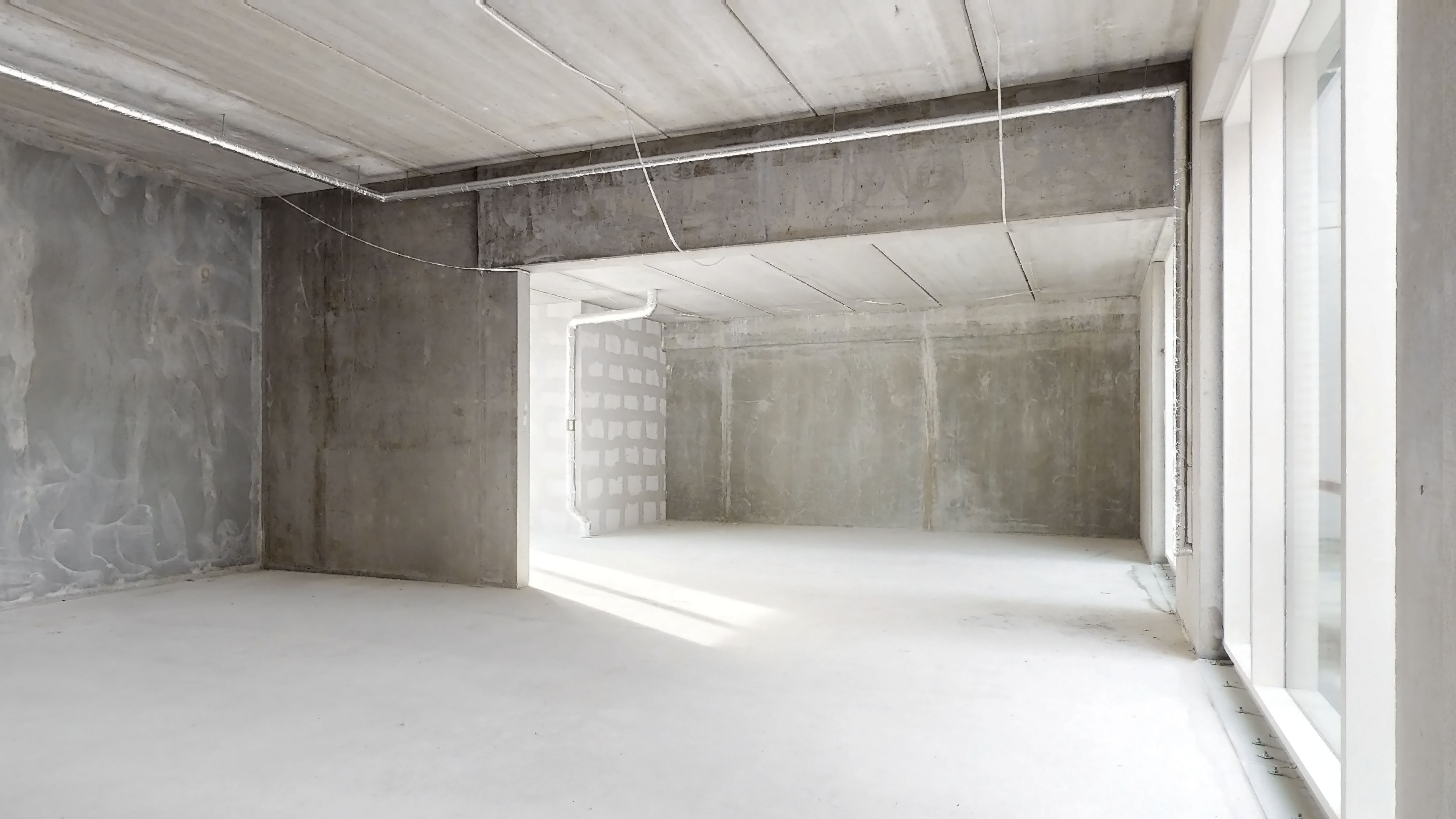 Et tomt rum med cementvægge og hvide gulve, hvor dagslys skinner ind gennem vinduet. Rummet er ubeboet og forberedes til