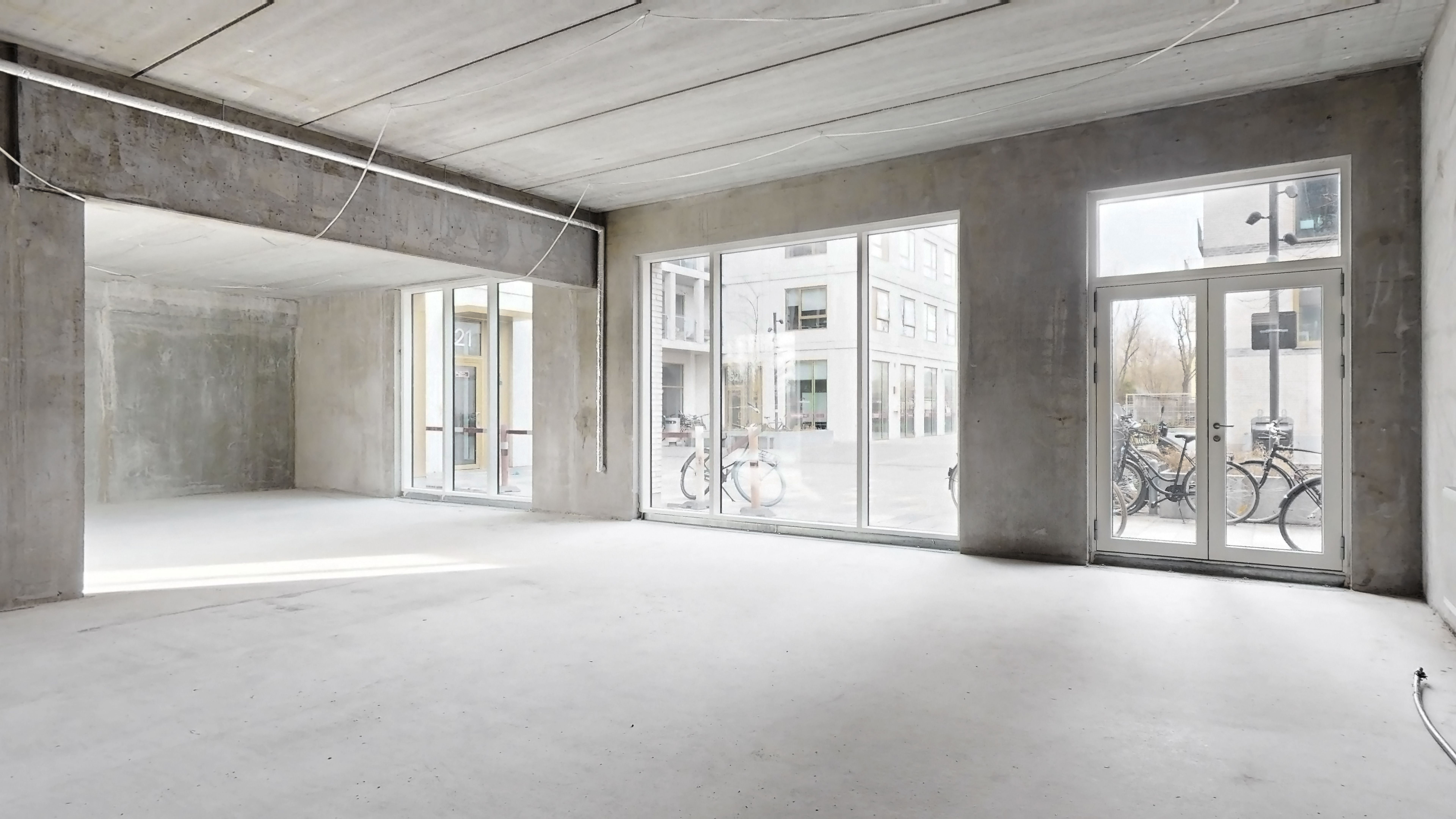 Store glasvinduer med dobbeltdøre i en ny bygning med en fredelig udsigt på gaden med cykler og bygninger