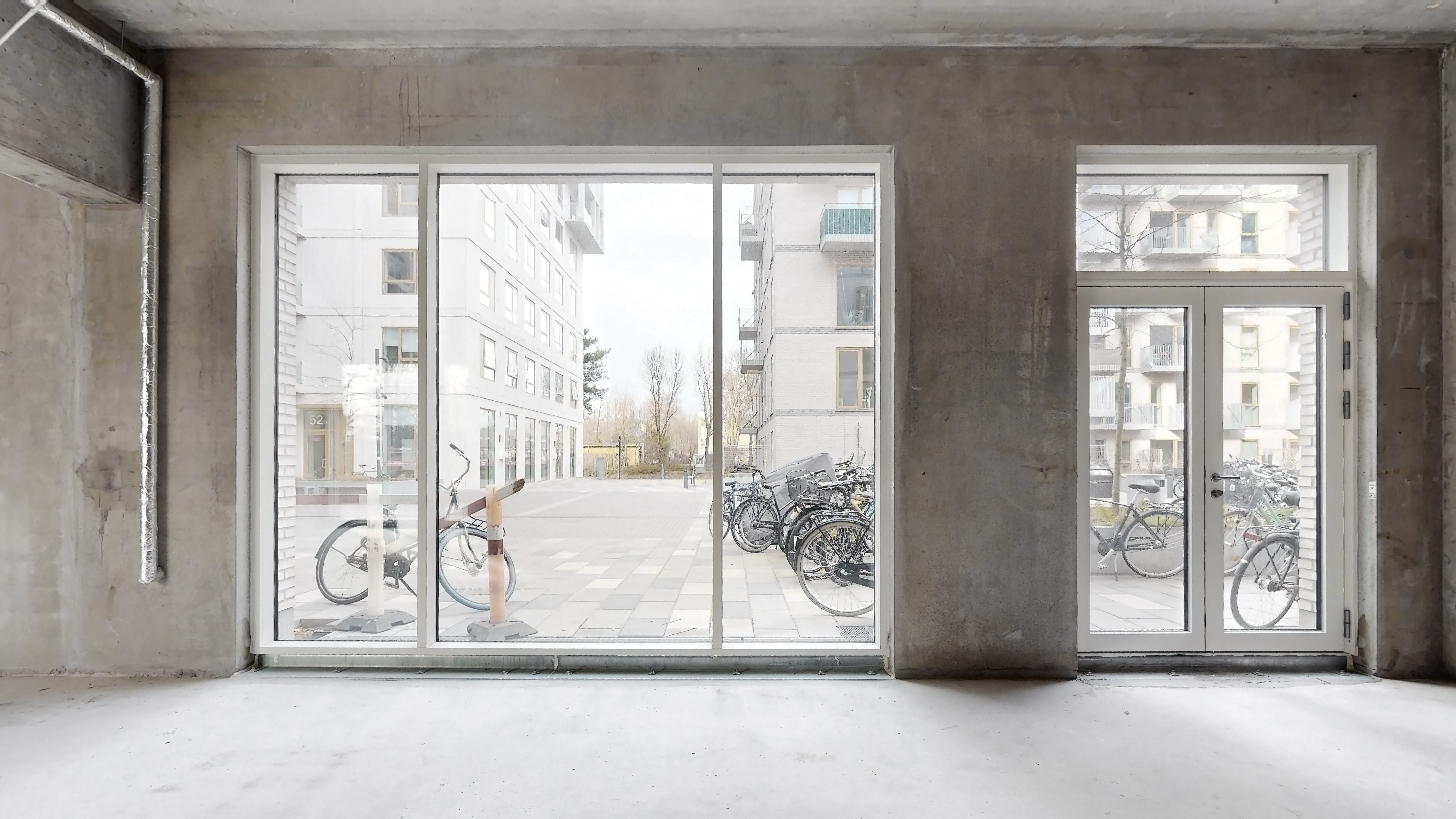 En tom og renoveret lejlighed med store vinduer og udsigt til søjler, parkeringsplads og en bygning med terrasser