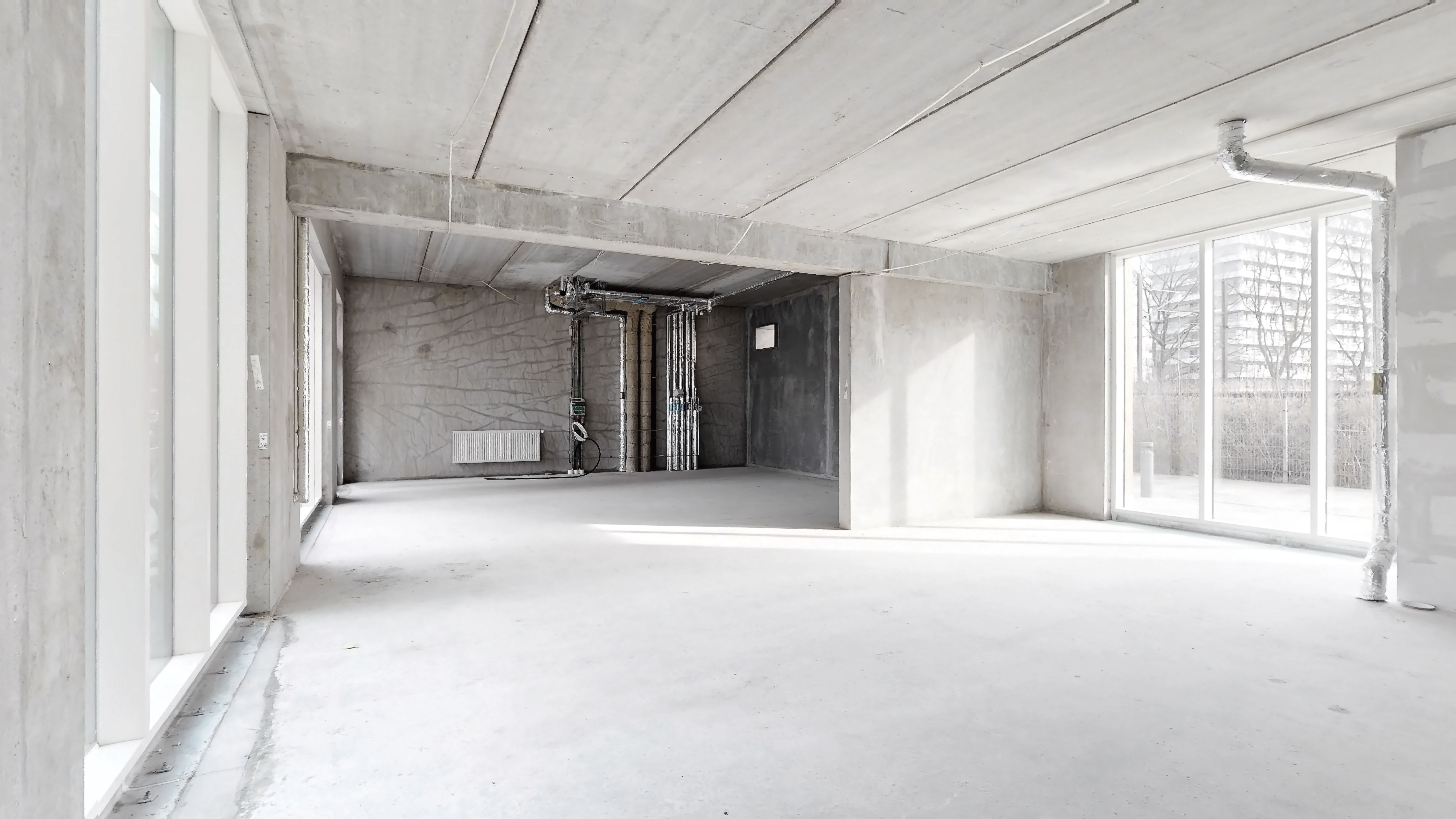 Et stort, ubeboet rum med hvidt loft og gulv og vinduer mod en bygning udenfor