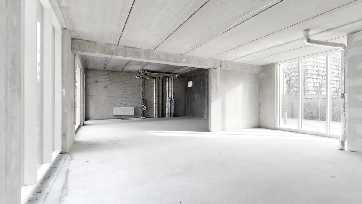 Et stort, ubeboet rum med hvidt loft og gulv og vinduer mod en bygning udenfor