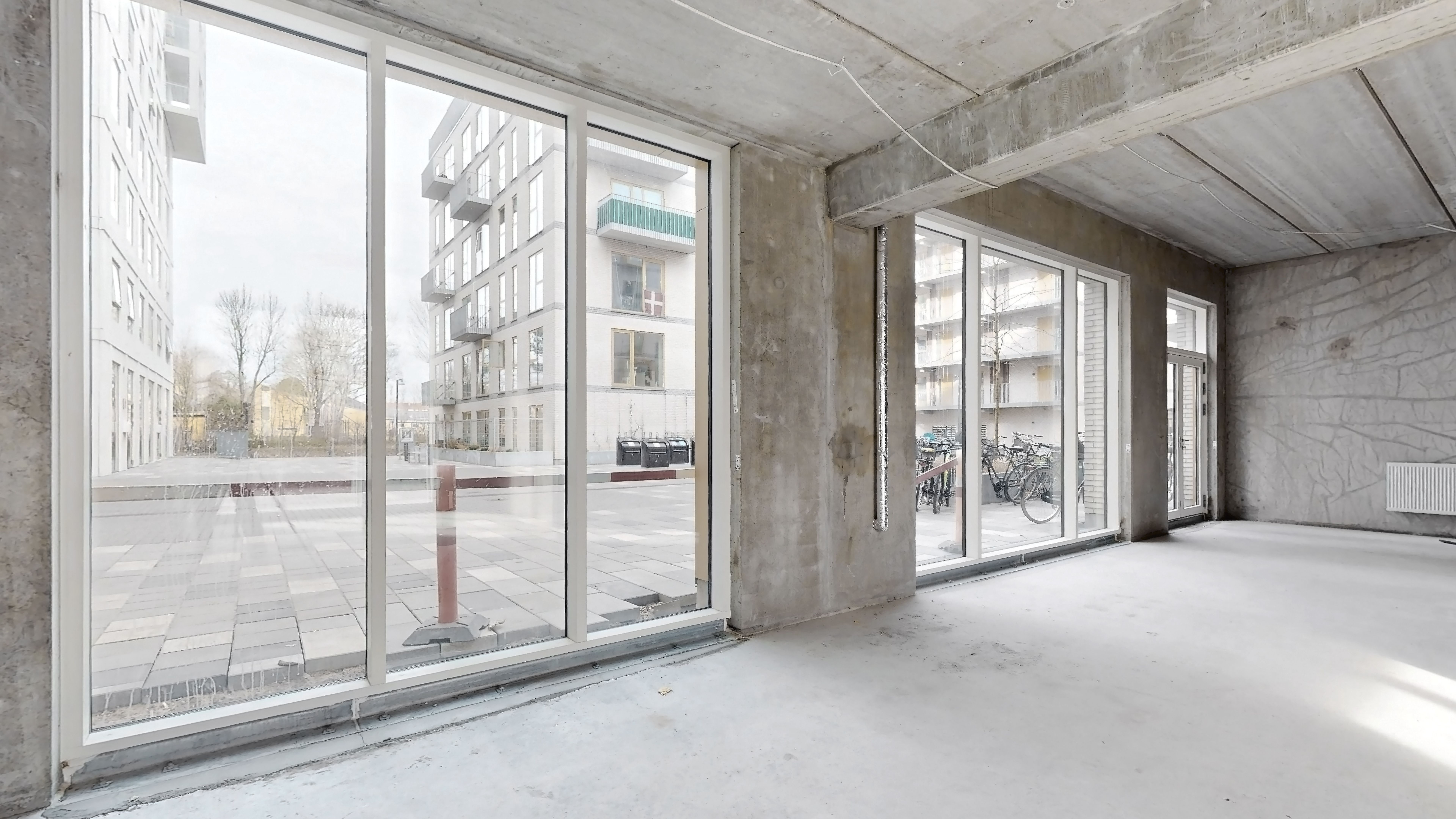 Et stort vindue med tre glasruder og et gulv med refleksioner af et byggeri og træer udenfor