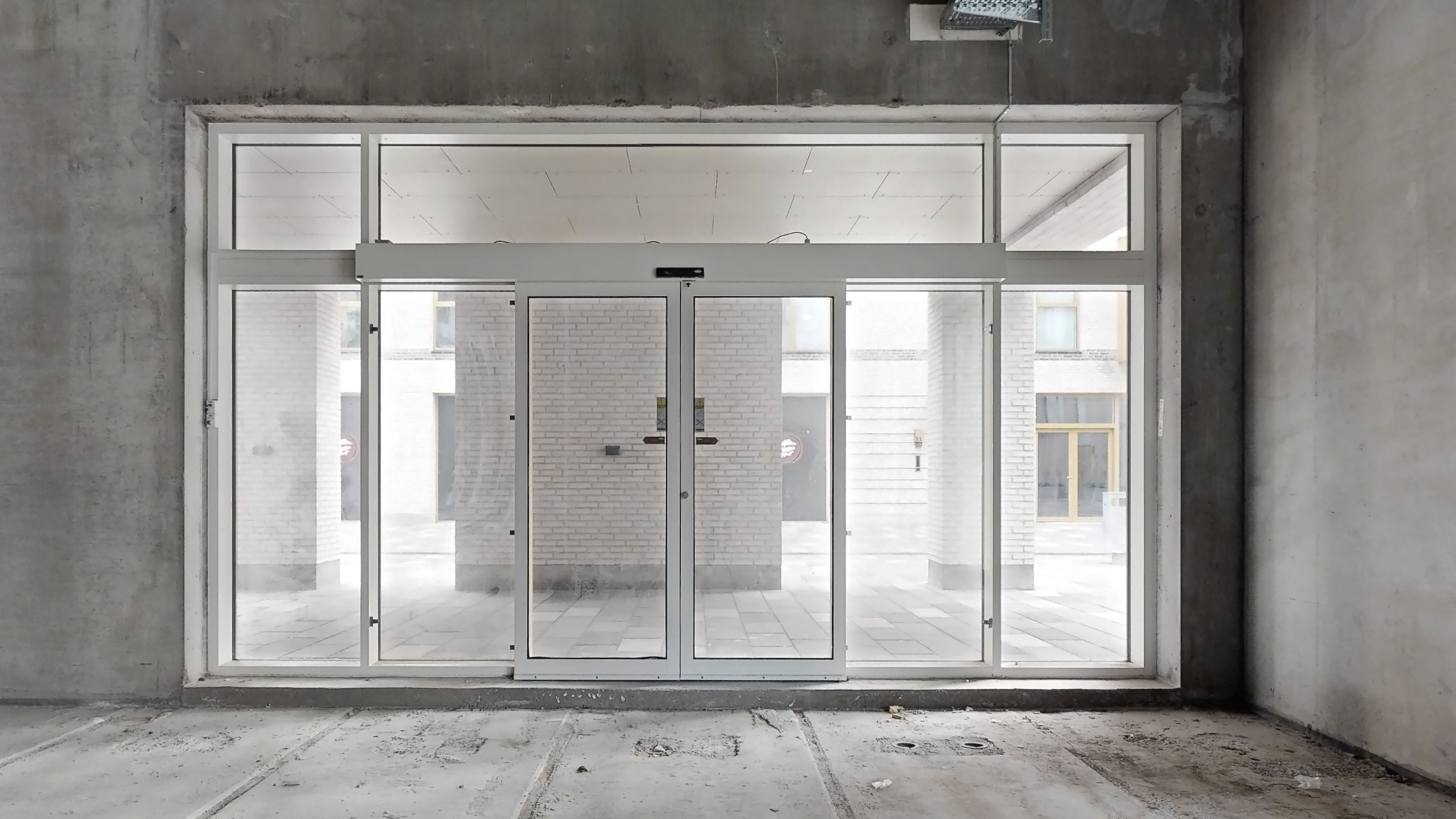 Et stort glas vindue med hvide rammer og to hvide skjemaer med glas lige midt i bygningen i Rødovre