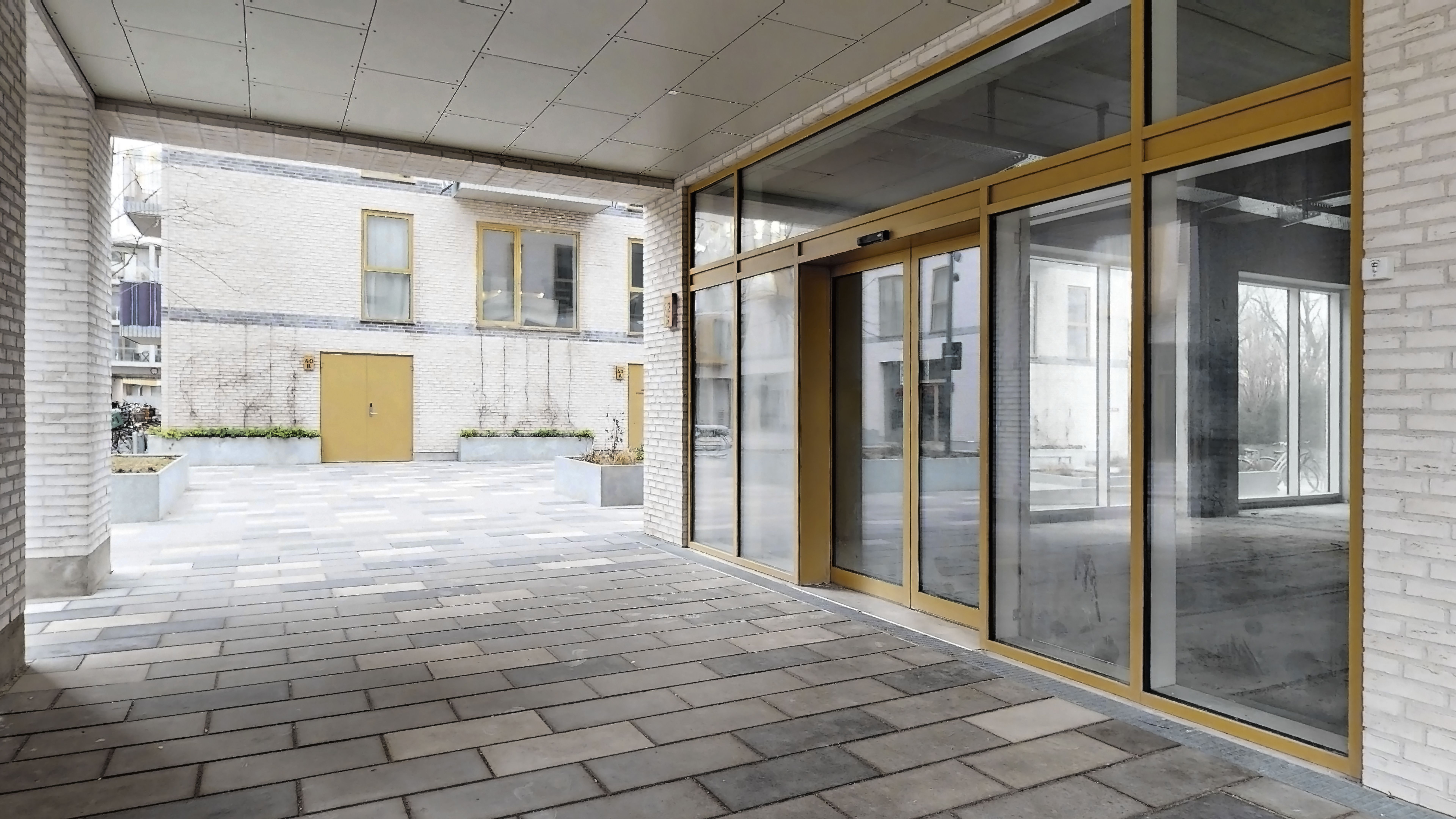 Glasdøre og højre søjle med to plantekasser og gult trædør i en gård med en forside til et højhus med flere vinduer