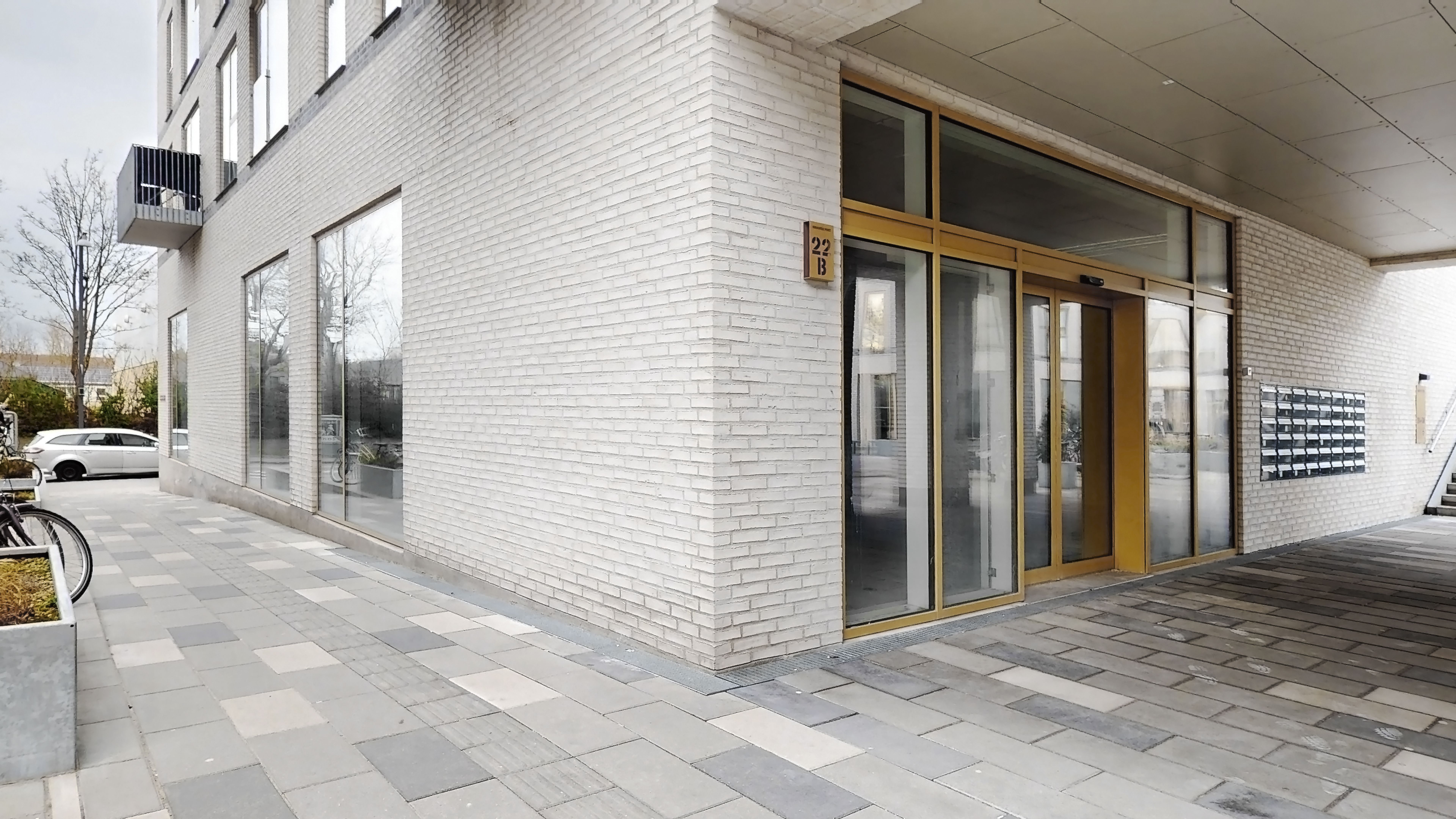 En hvid mur med glasdøre og -ruder og nummer 22B på facaden, med et stel og en cykel foran