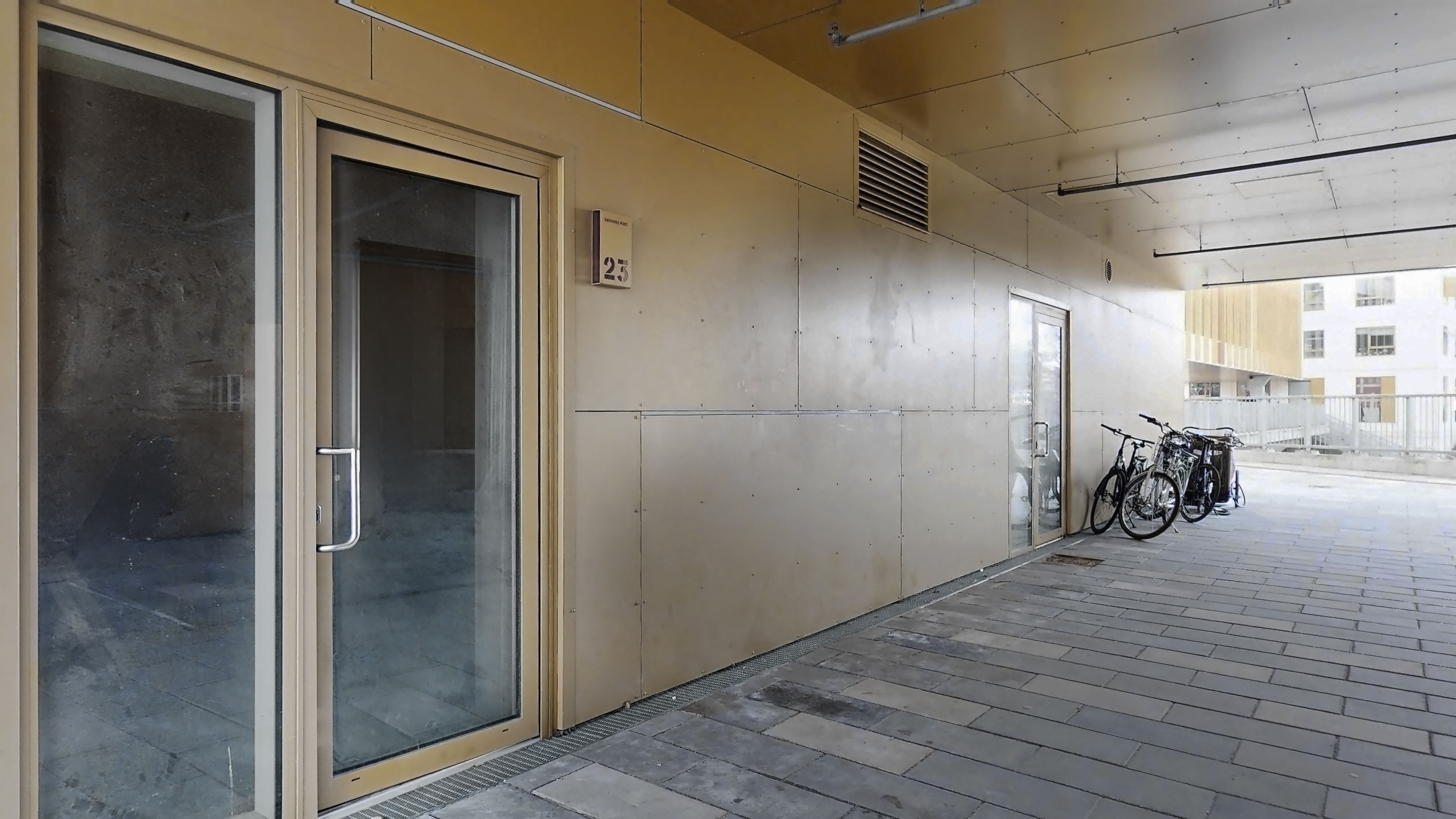 Korte gange med nummer 25 og glasdøre med nummer 25 samt en cykelparkering på højre side med tre cykler og et sted at hænge