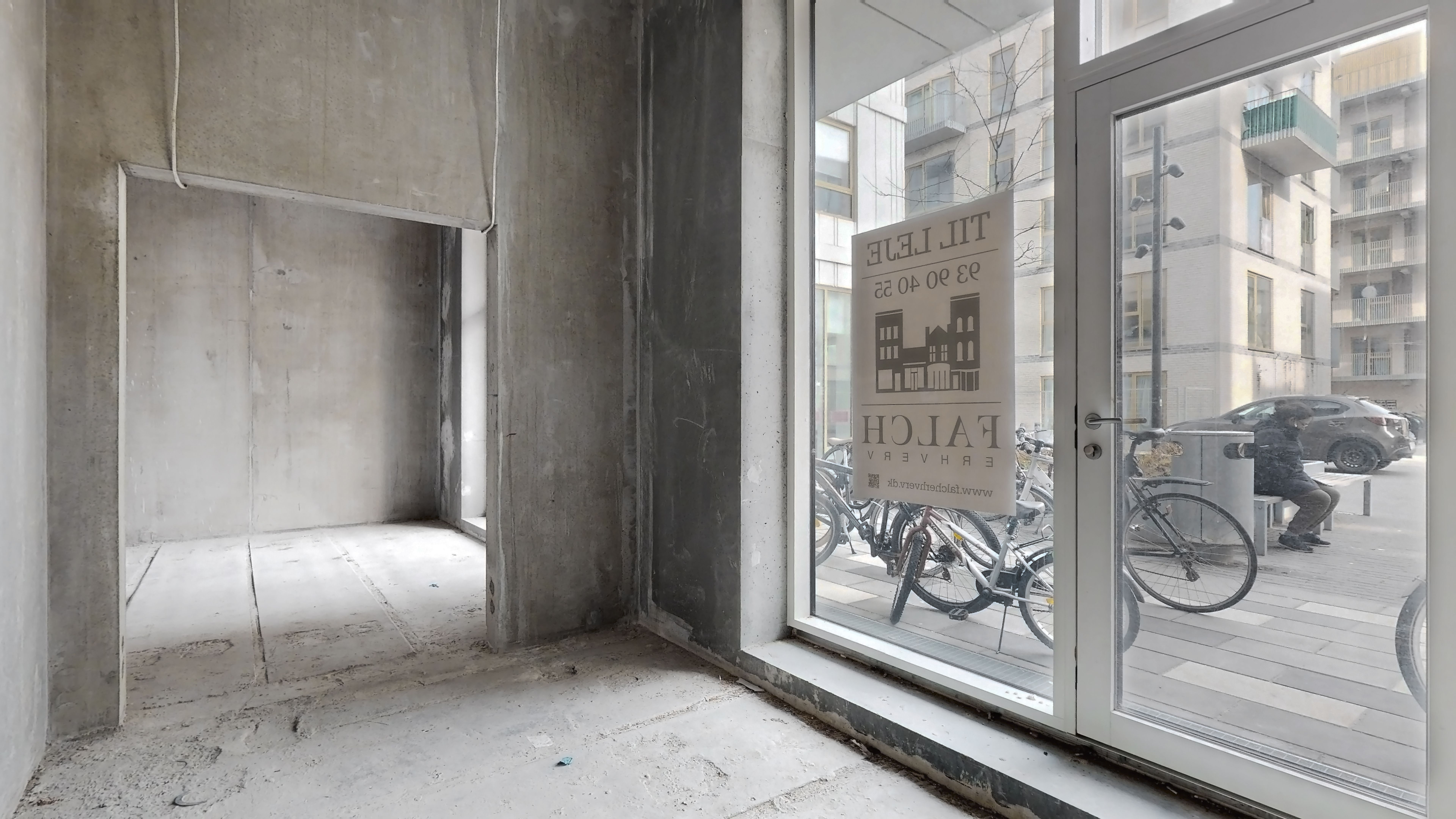 Udstødet lokale i en ny bydel i Rødovre med et skilt, der siger "Flat for rent". På gaden udenfor parkerer biler og cykler,