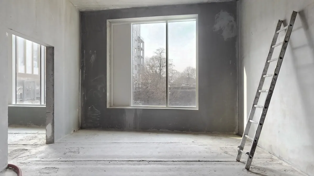 En tom værelse med en metal stige mod væggen og et vindue, der vender ud mod flere bygninger og træer