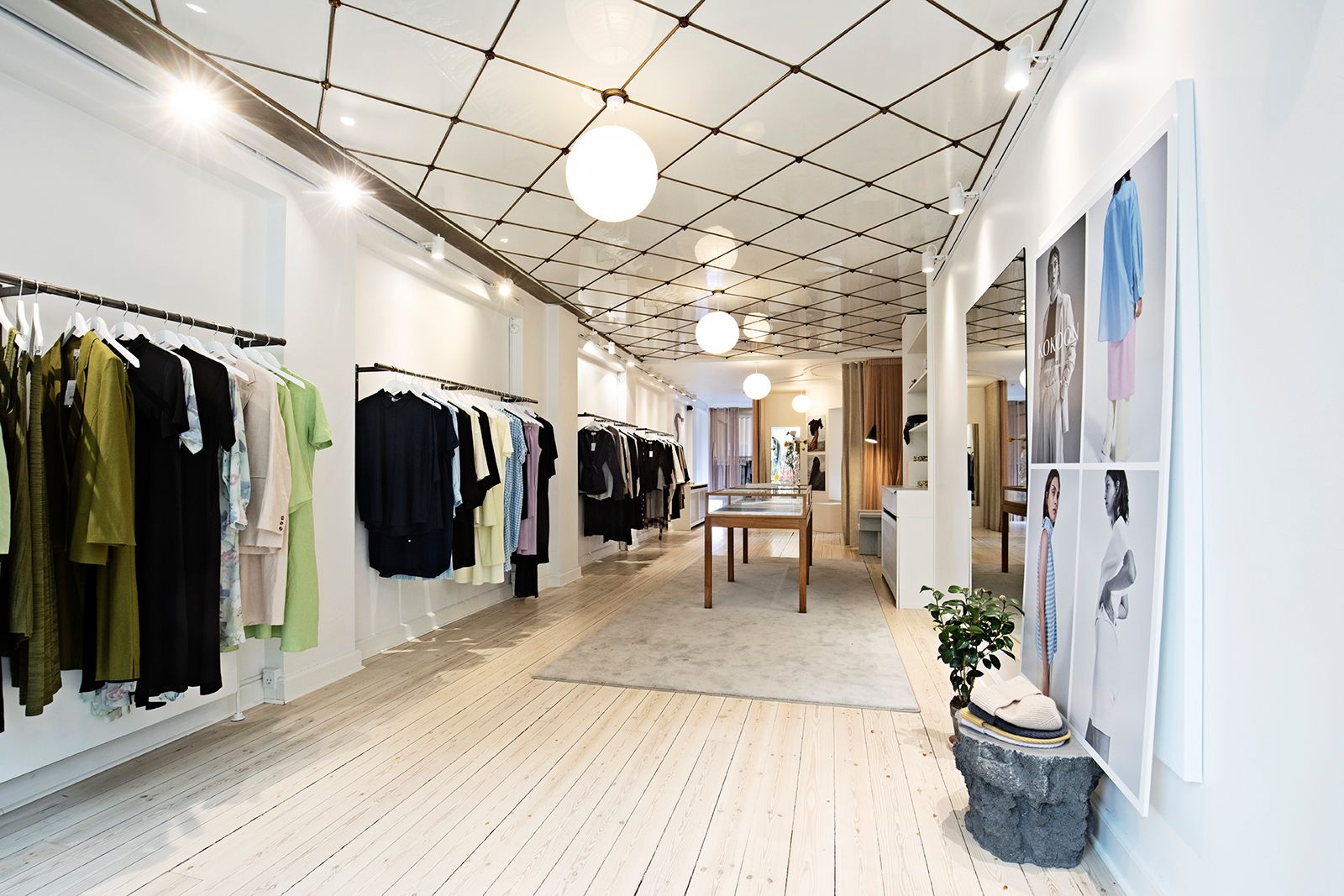 En køkken med hvide vægge, lyse loftslampe, tøj i garderobeskabe og et foto på væggen med et træbord og en plante