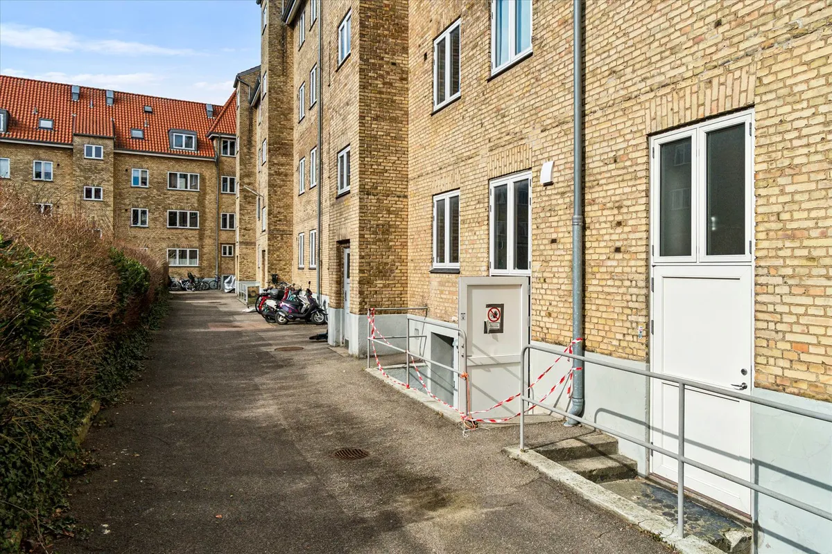 Et lejlighedshus i Brønshøj med røde tag og hvide ruder og en scooterparkering med sikkerhedsbånd