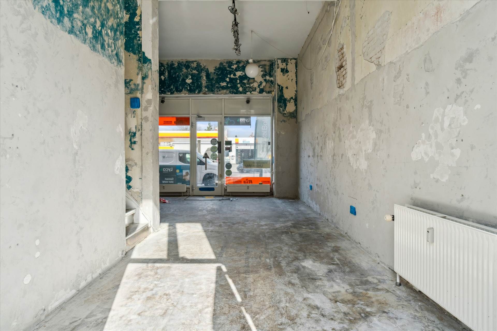 Ledig butik med skrald i gulvet og slettede vægge ved en vej og Shell tankstation i baggrunden