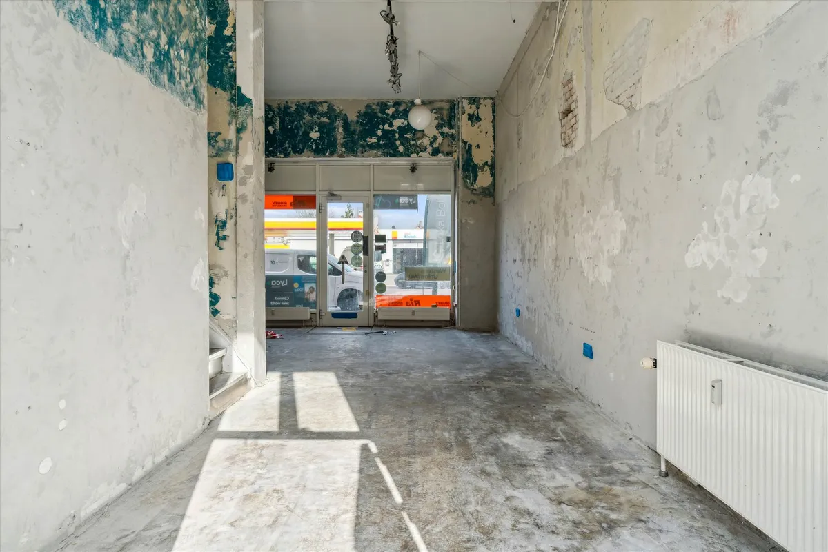 Ledig butik med skrald i gulvet og slettede vægge ved en vej og Shell tankstation i baggrunden