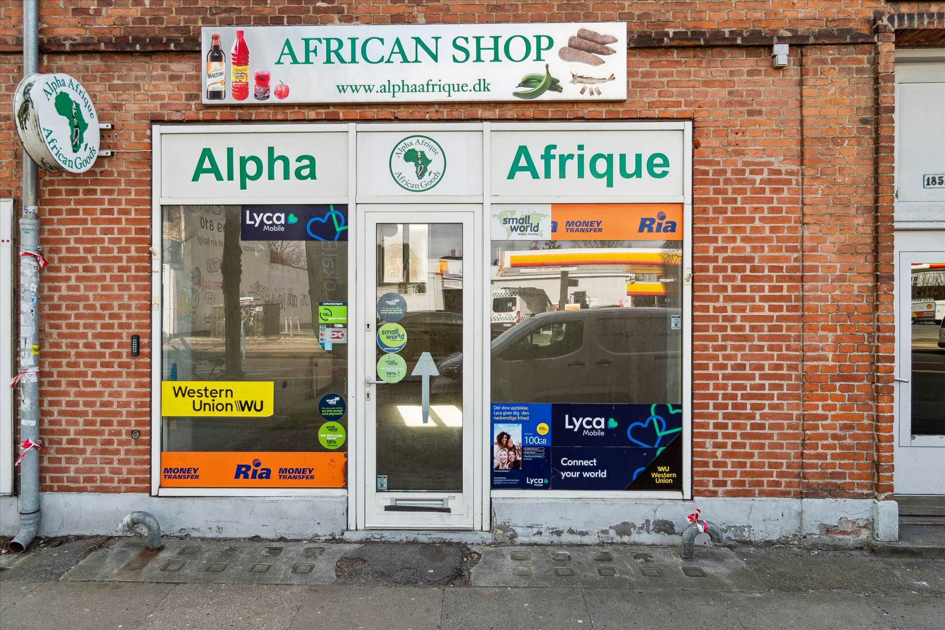 Afrikansk butik med skilte og reklamer på facaden, vinduet med Western Union, Ria og Lyca Mobile reklamer og logoer samt
