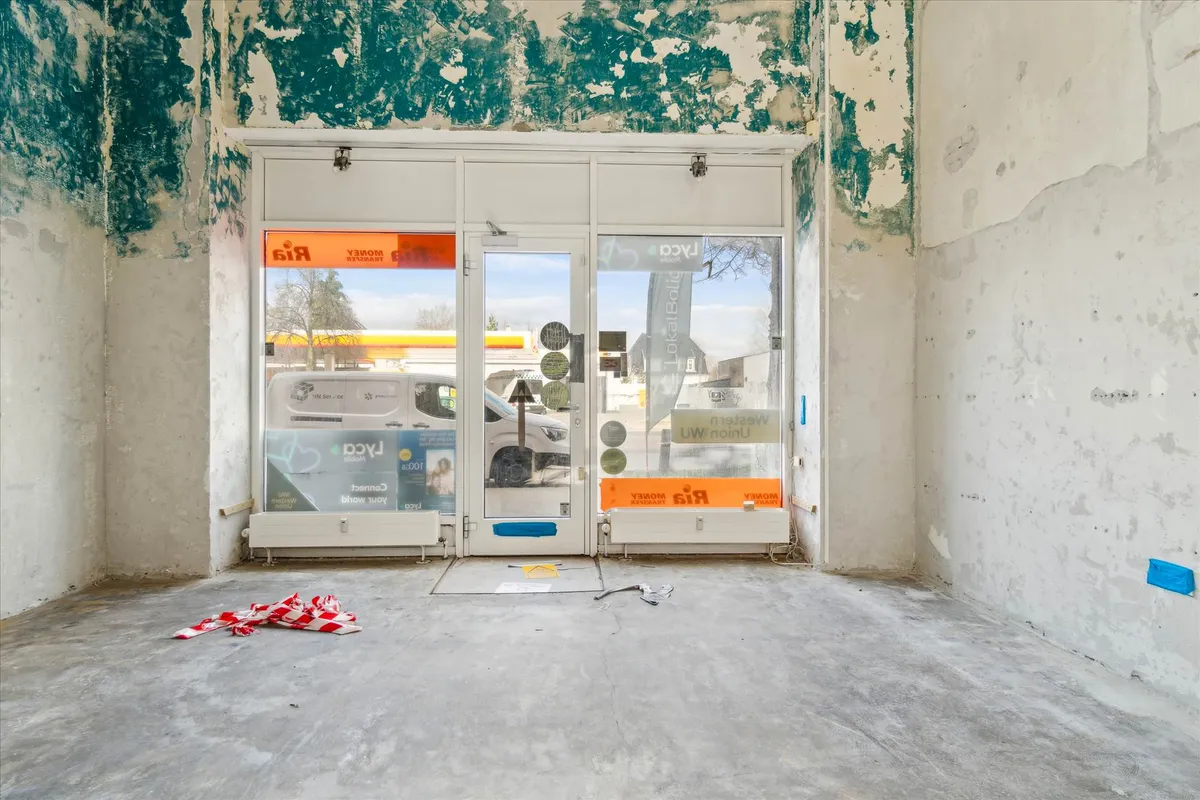 Ledig butikslokal med glasdøre og udstillingsvindue. Byggeforløbet er i gang med hvide vægge og gule gulve. Butikken er tæt