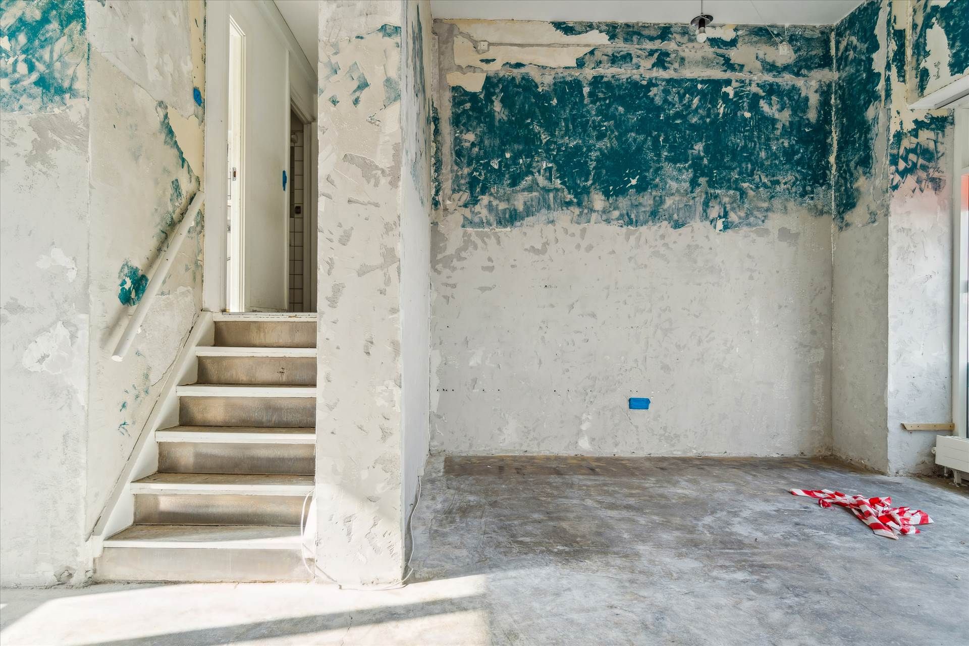 En ubeboet stue med et forfaldent loft og vægge. Der er et trin til en trappe med hvidt gelænde. Væggen er slettet med