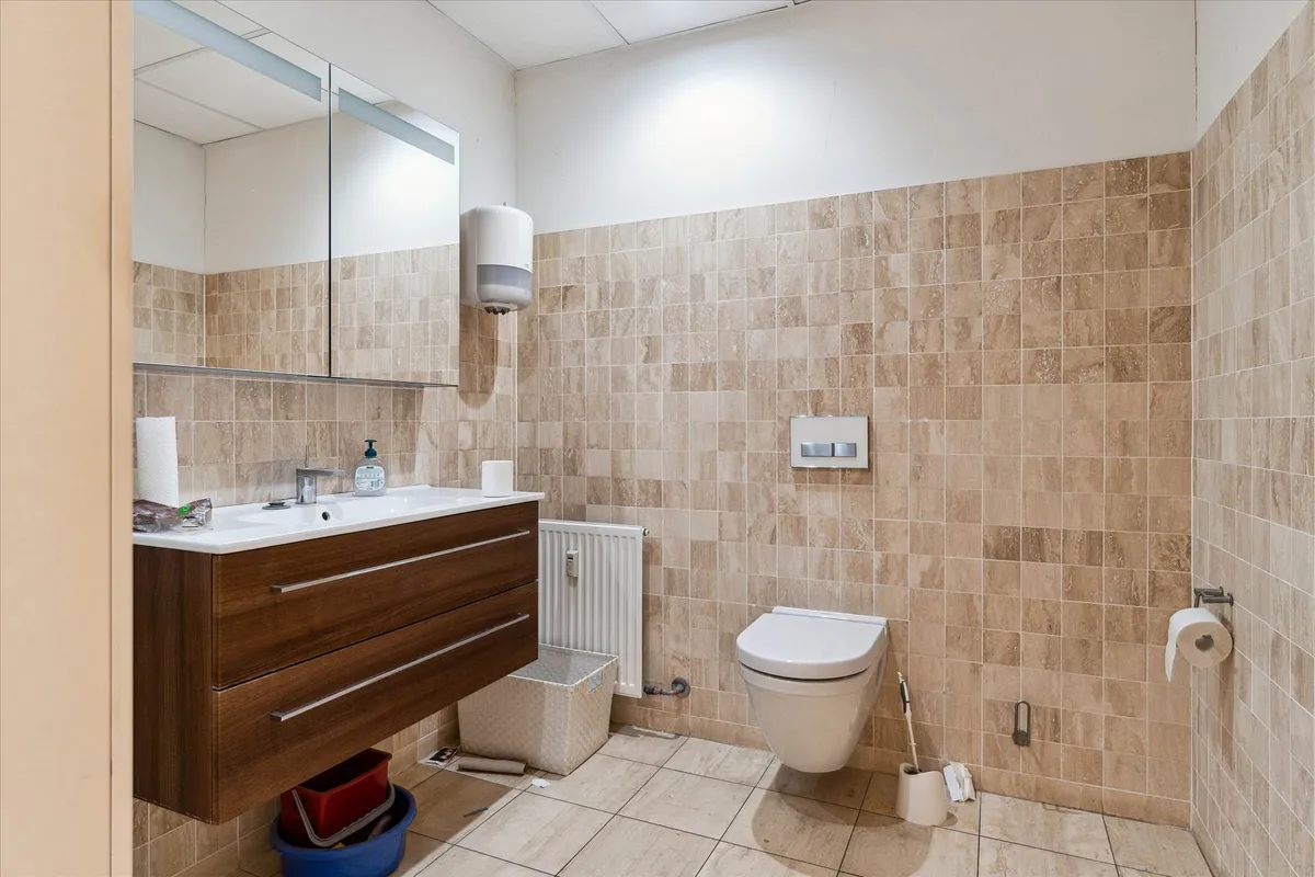 Lækkert badeværelse med dobbeltvask, håndklædetørrer og toilet i beige og brune kakeloverflader