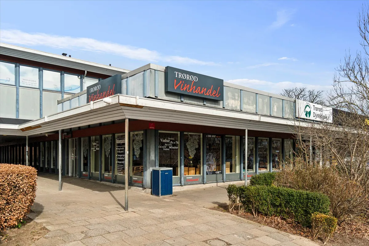 Forretningslokaler med Trorod Vinhandel, Trorod Dyrklinik og Vinbar på en hjørnebygning med grønne buske og træer