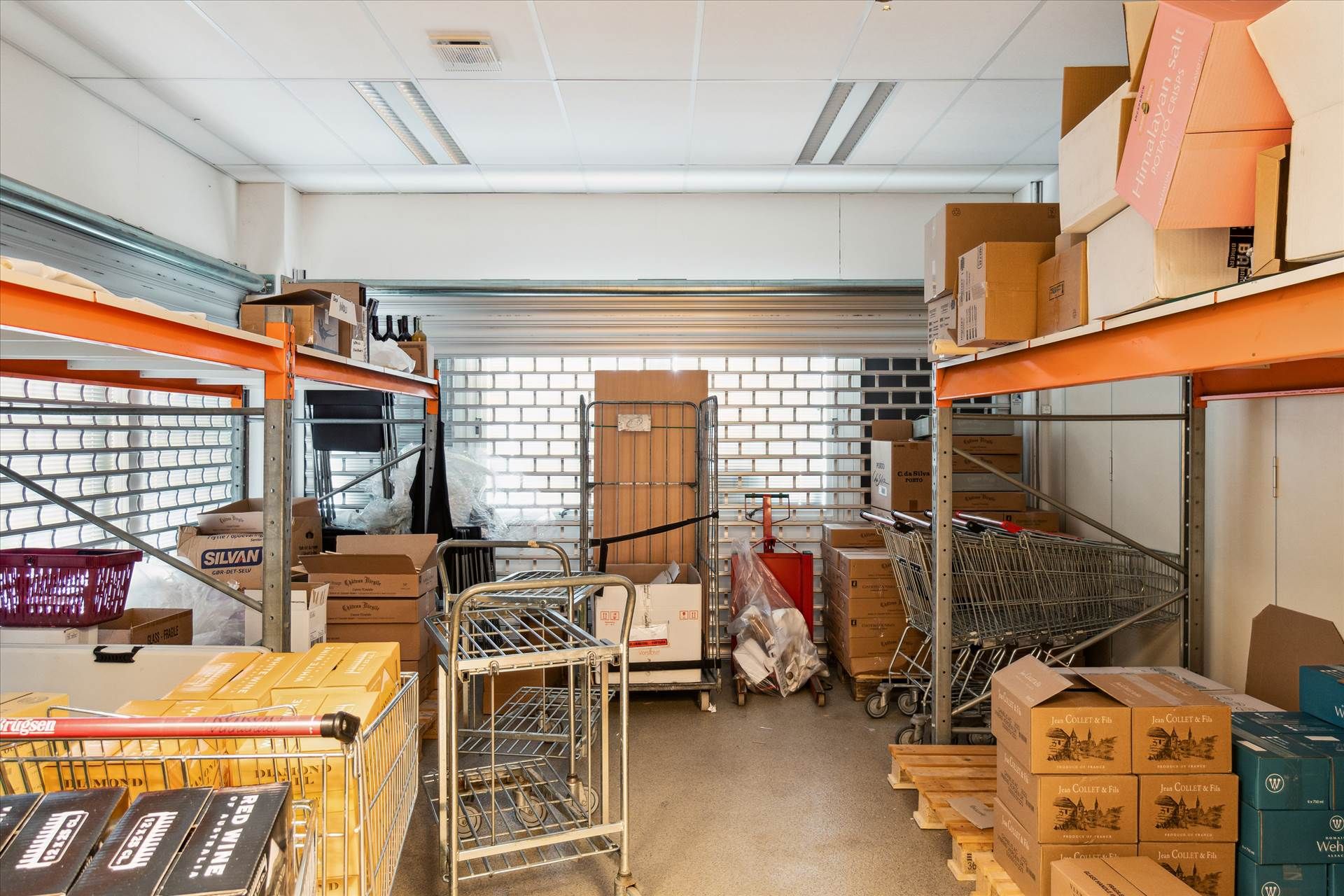 Lager med store og små kartoner, der er opstillet på hylder og gulvet, samt to kørekurve og to indkøbsvogne